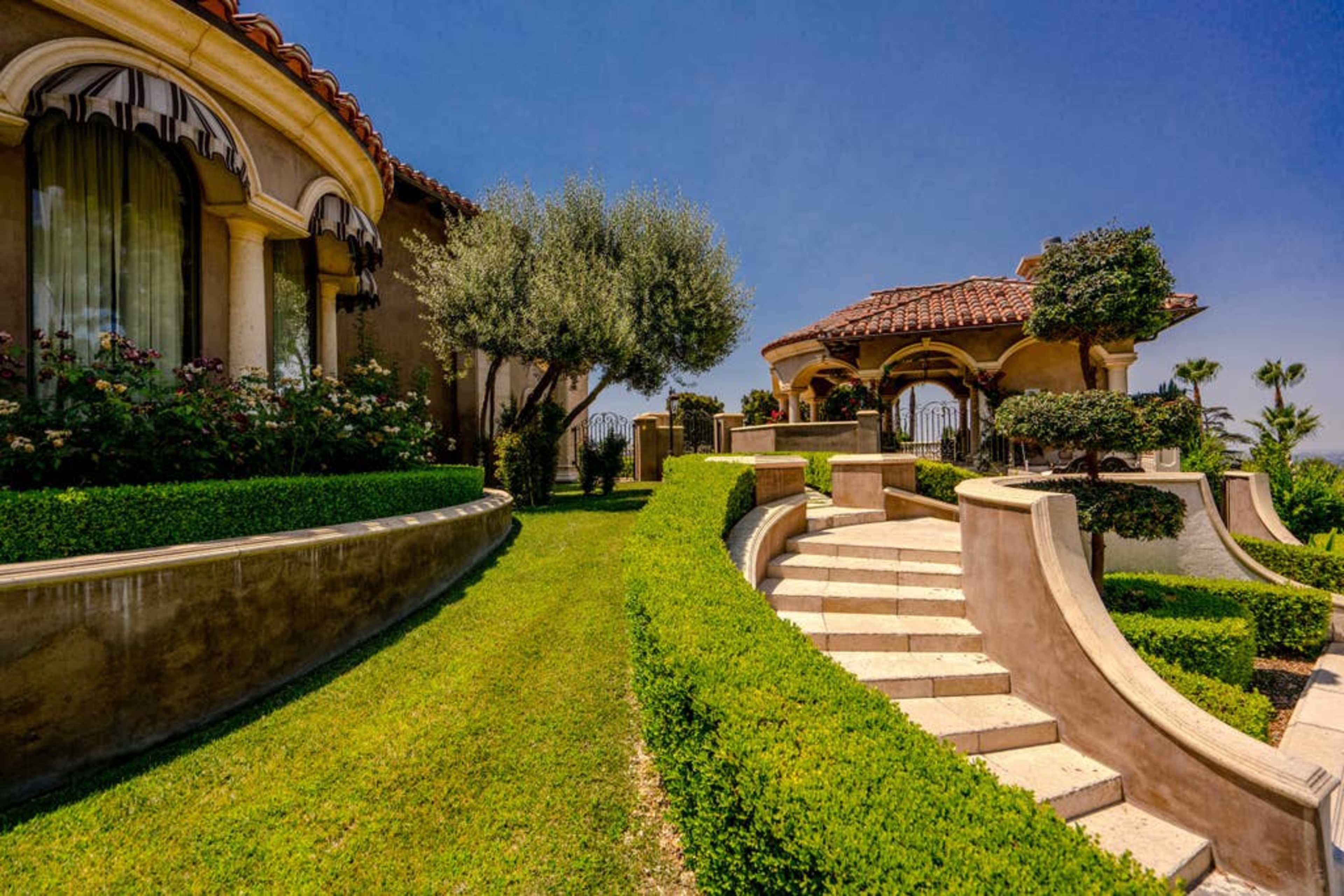 The image shows a landscaped garden with a stone staircase leading up to a gazebo and a building with arched windows.