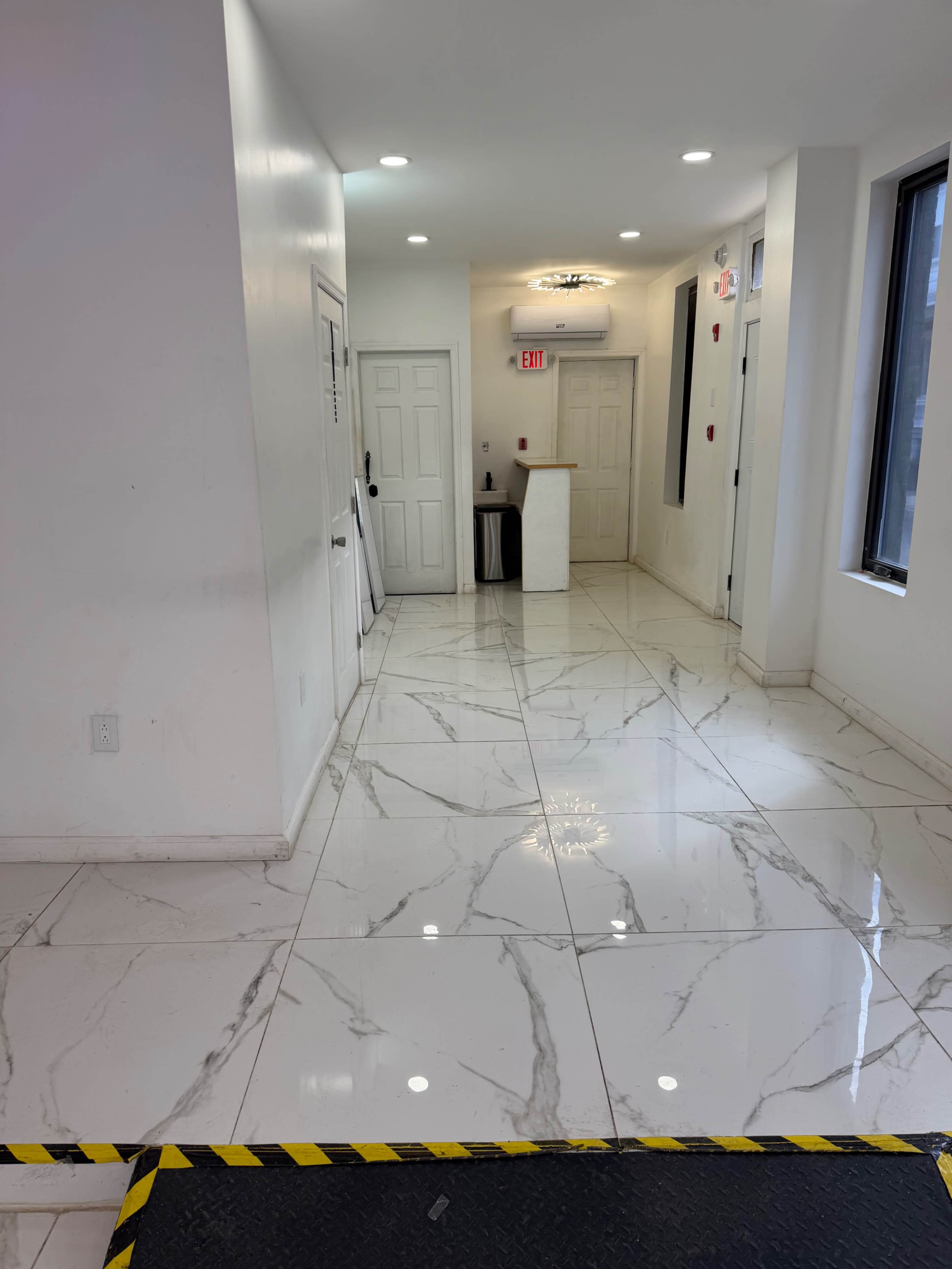 The image shows a hallway featuring glossy white marble flooring, white walls, and several doors leading to other rooms.