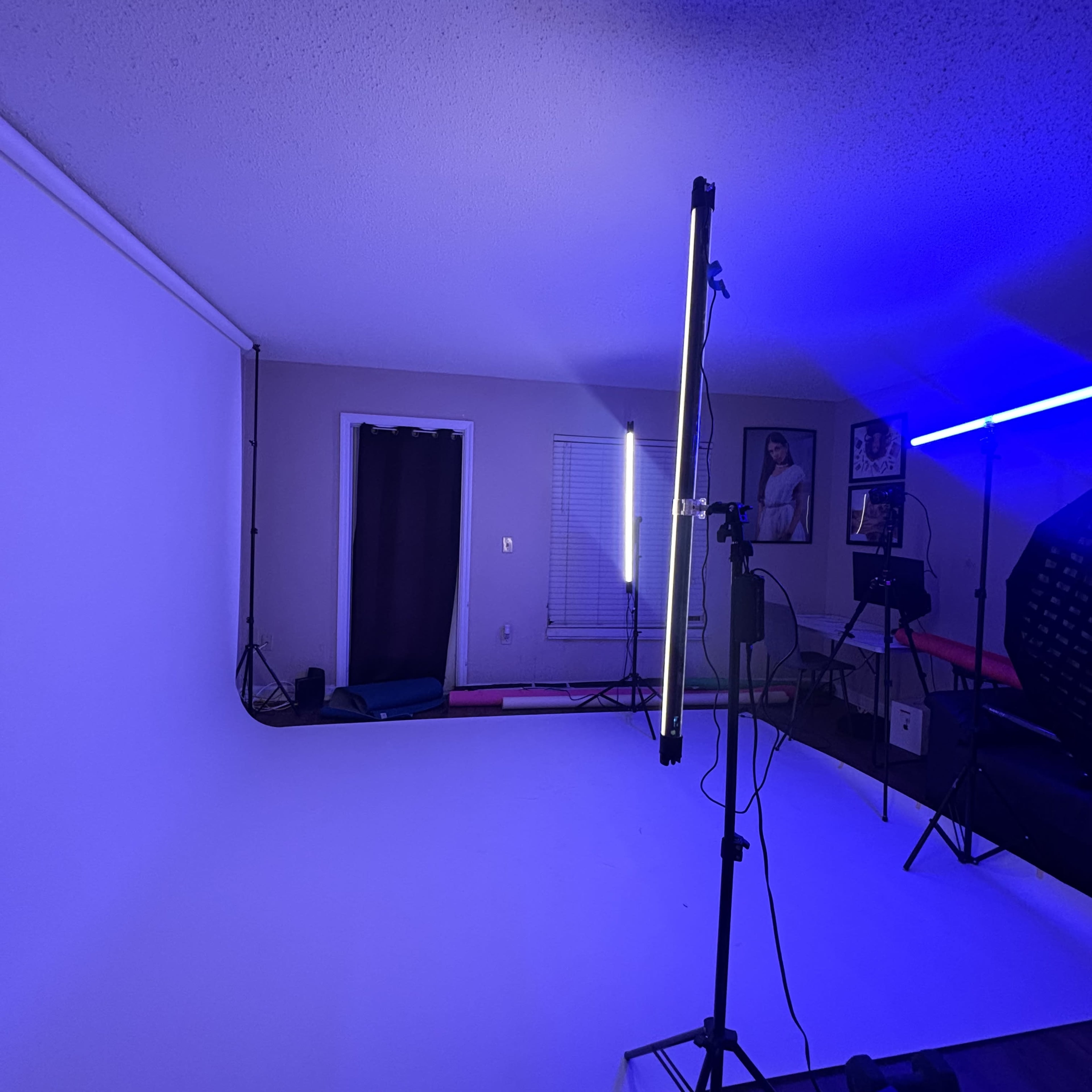 The image shows a photo studio with a white backdrop, lighting equipment, and a partially visible portrait on the wall.
