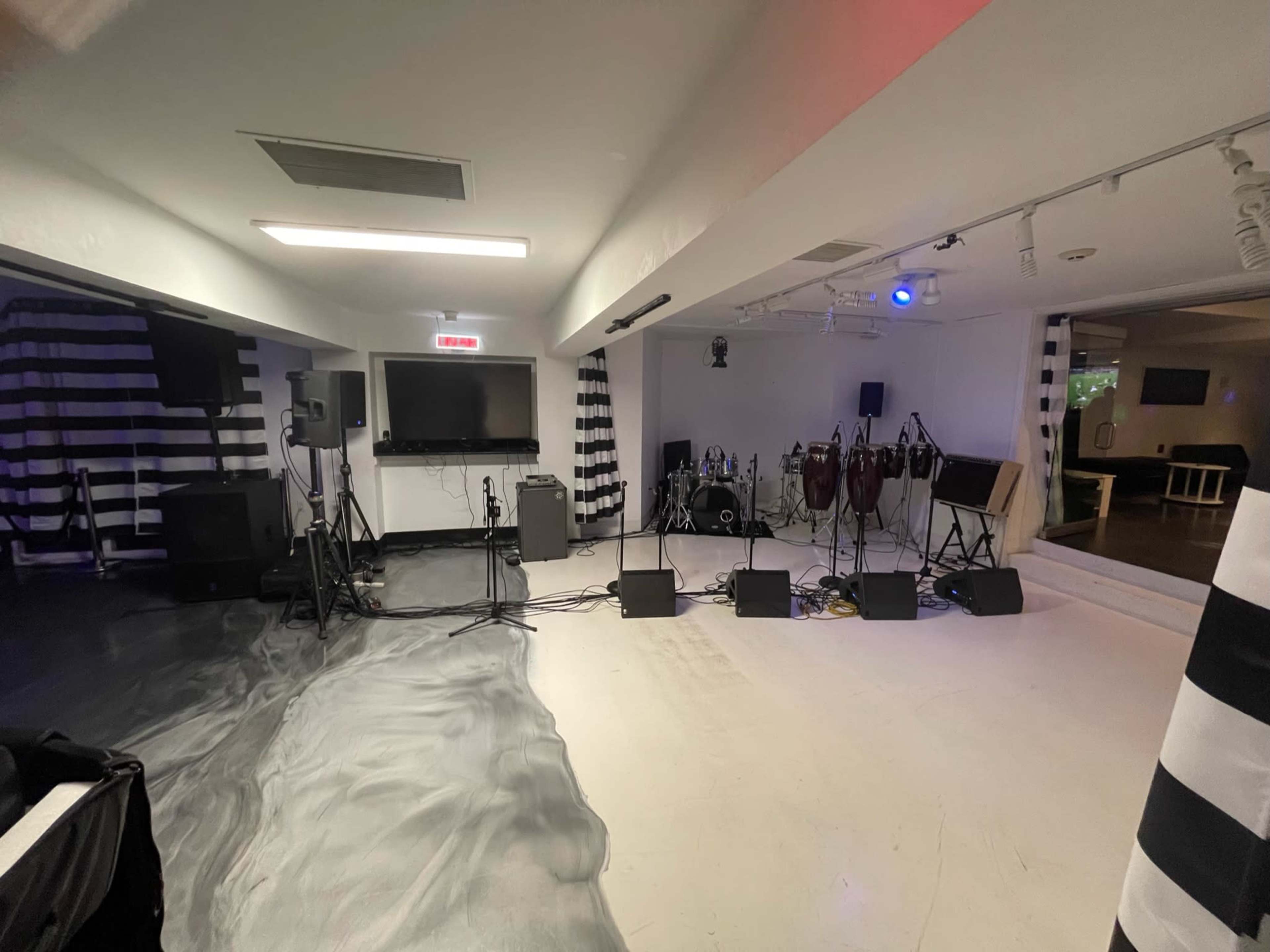 The image shows a performance space equipped with sound equipment, musical instruments, and black and white striped walls.