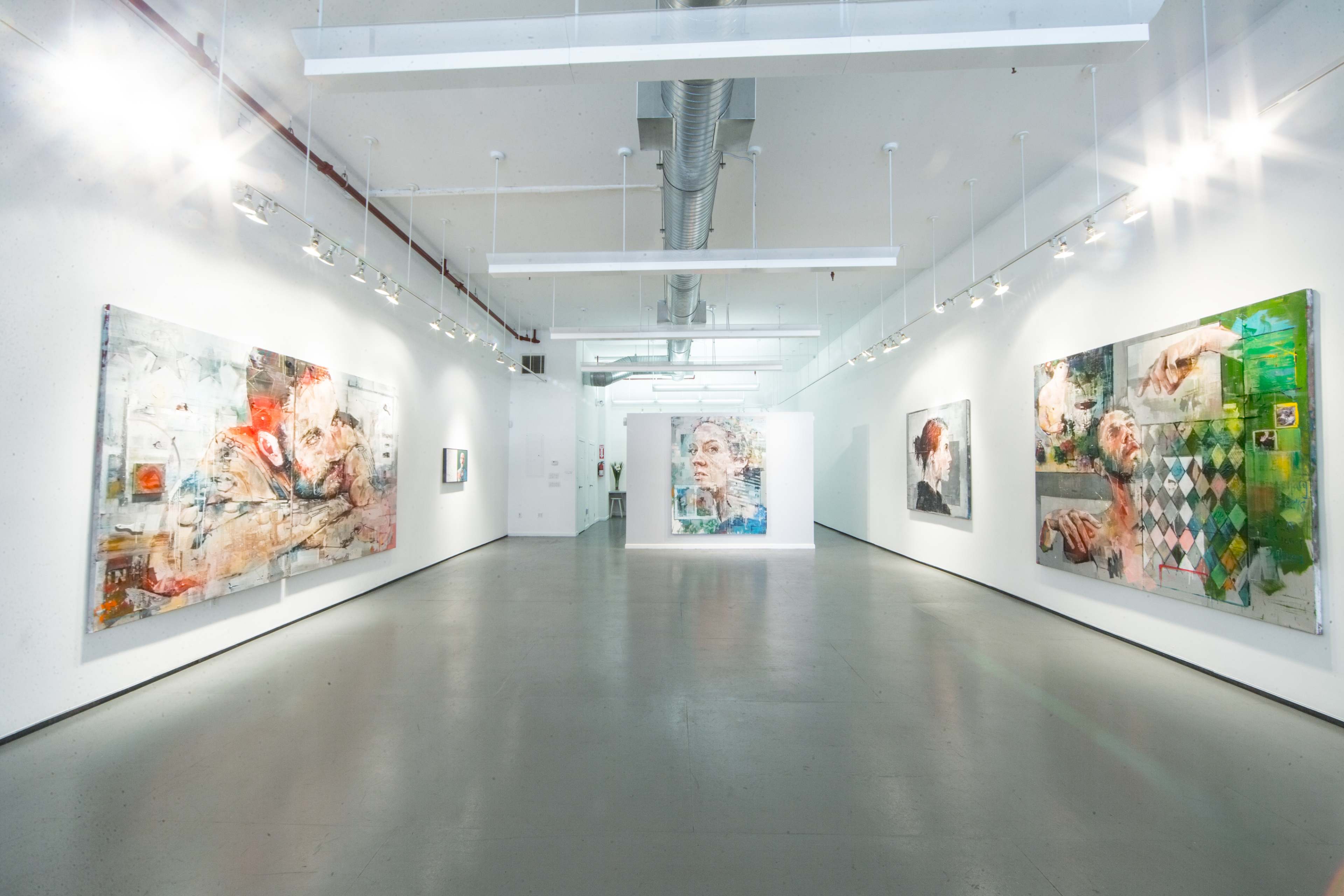 A spacious art gallery with large, abstract paintings displayed on white walls and ample overhead lighting.