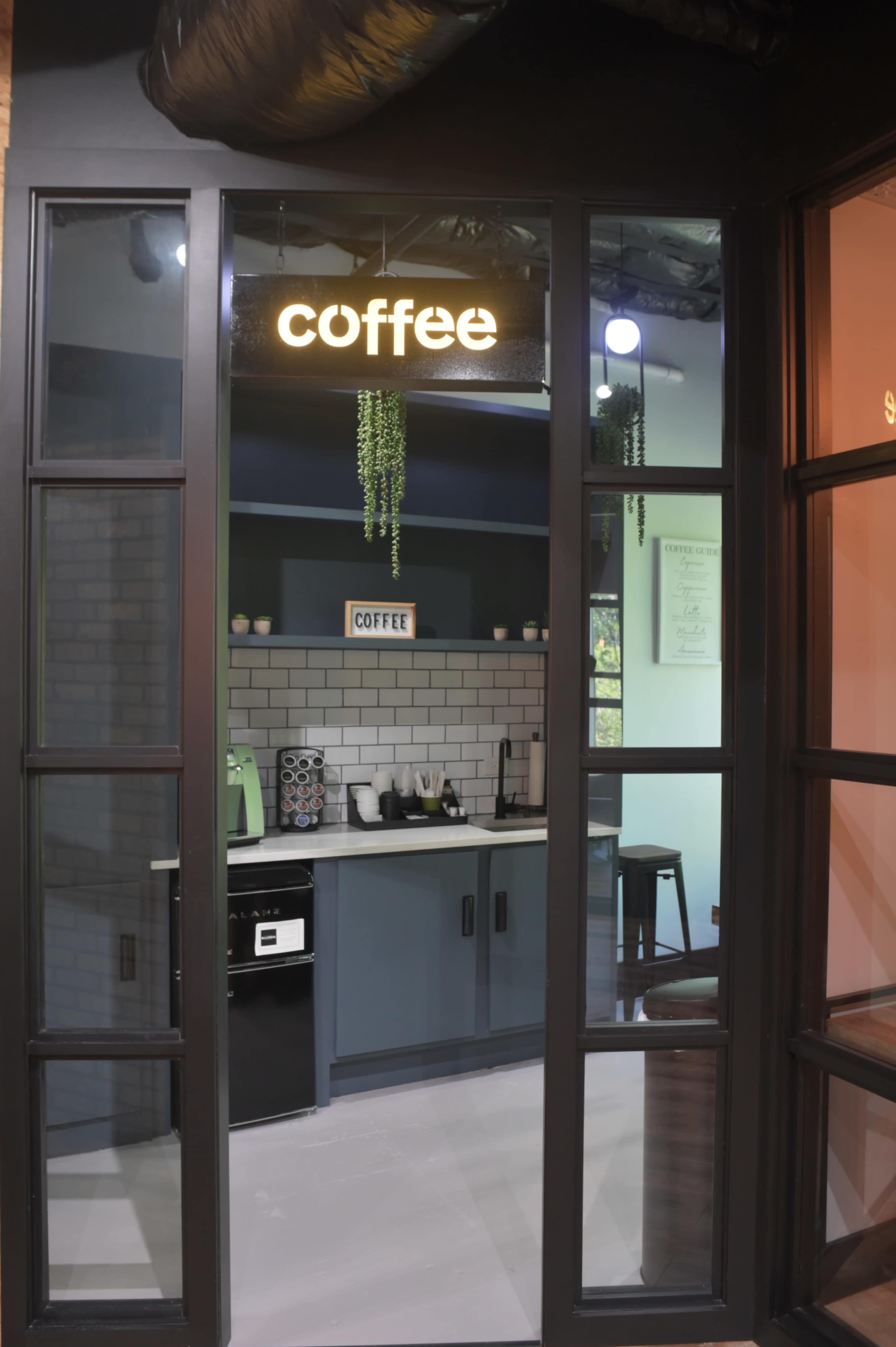 The image shows a coffee counter with a brick backsplash, various kitchen appliances, and a sign labeled "coffee" hanging above.