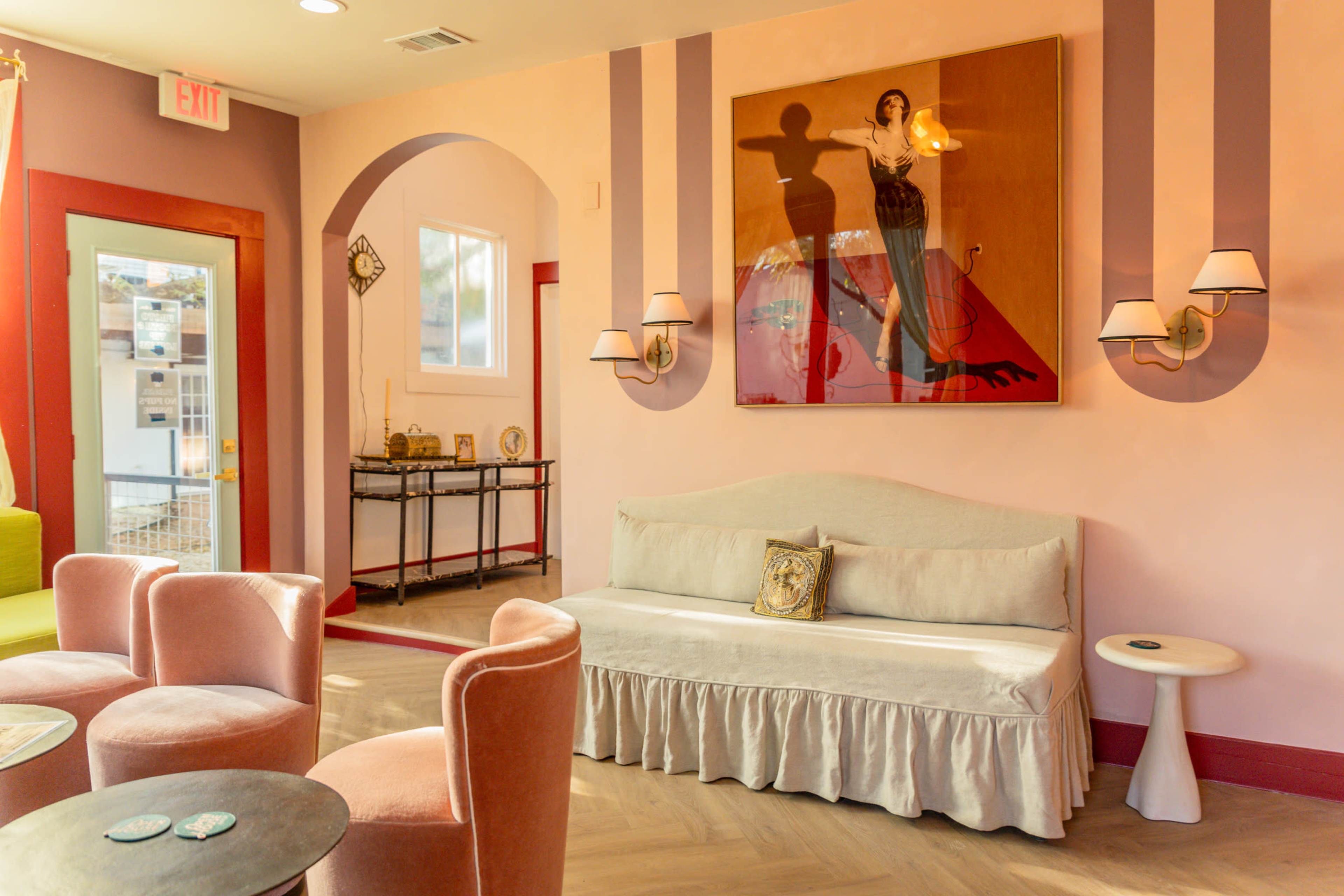 A stylish interior room with a pink and red color scheme, featuring a sofa, several chairs, and a large framed artwork on the wall.