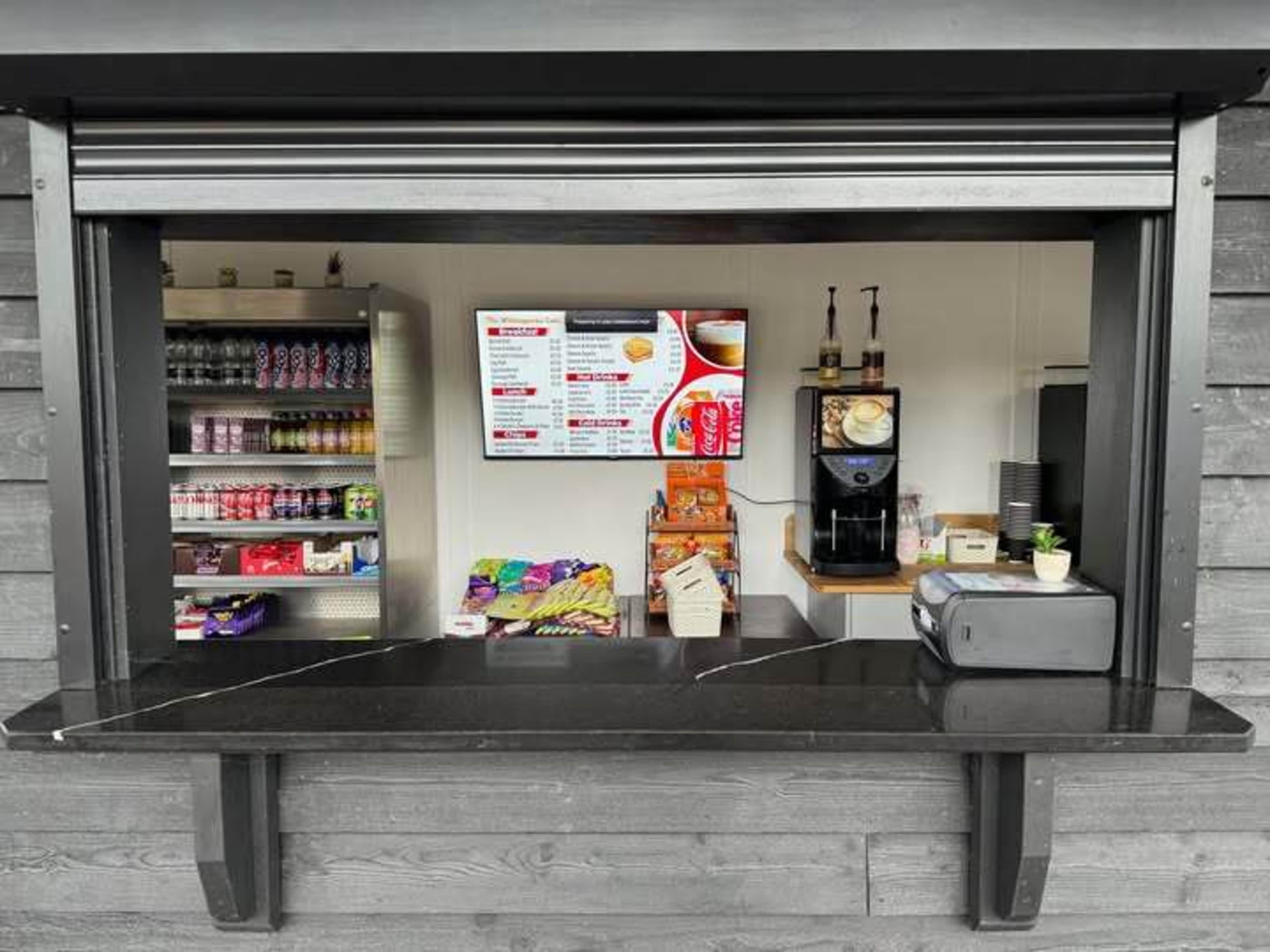 A food and beverage kiosk features a menu display, shelves stocked with drinks and snacks, and a coffee machine.