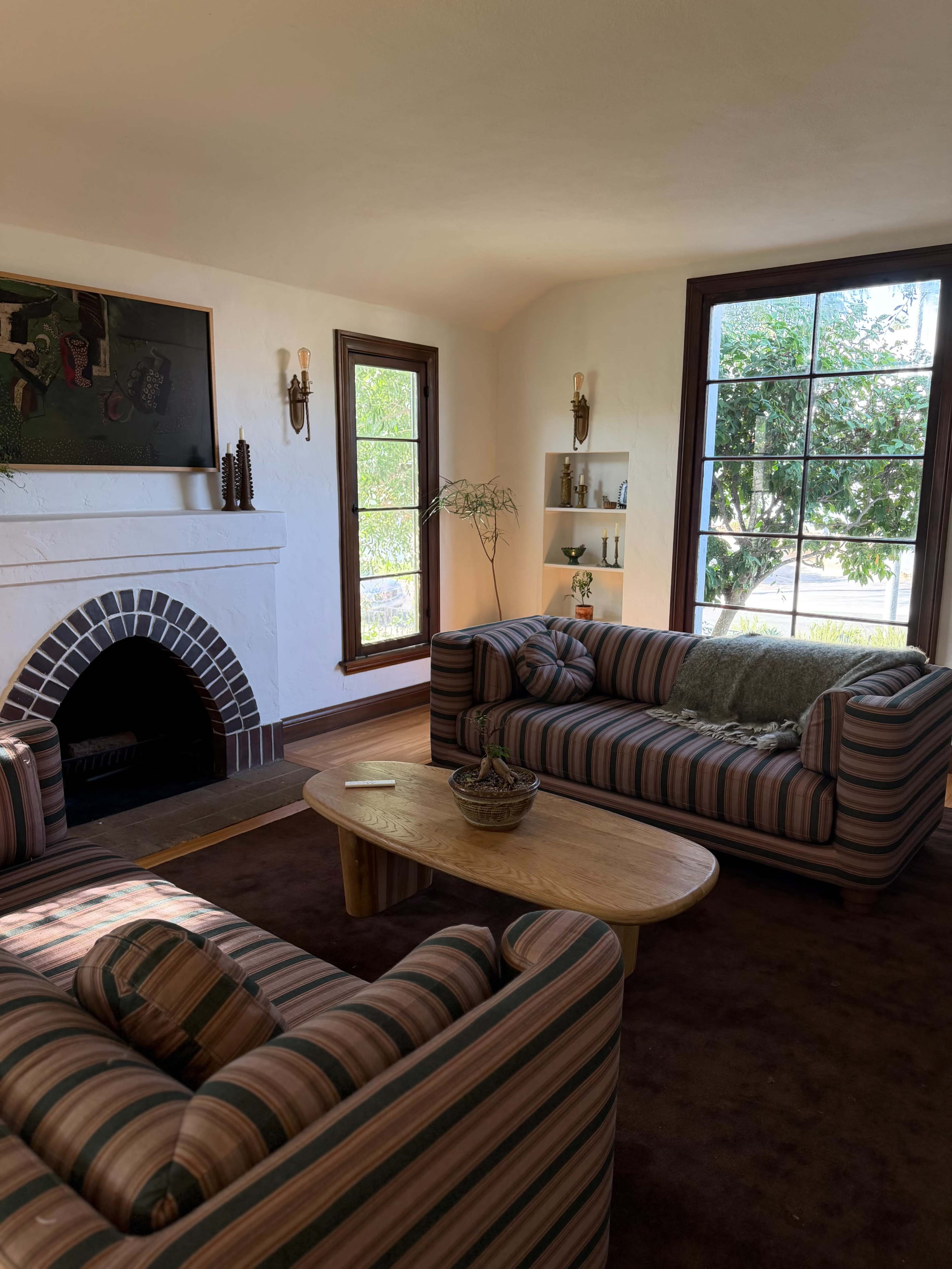 The image shows a living room with two striped sofas facing a wooden coffee table, and a large window allowing natural light to fill the space.