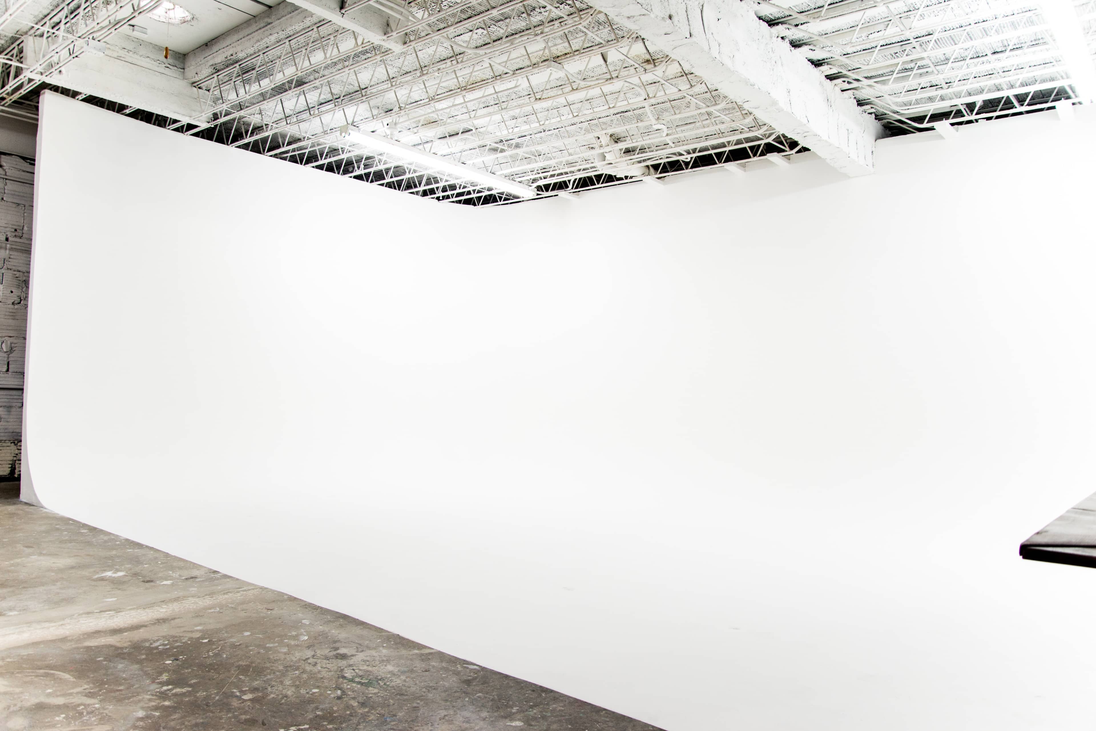 An empty photo studio with a large, white backdrop and a concrete floor.