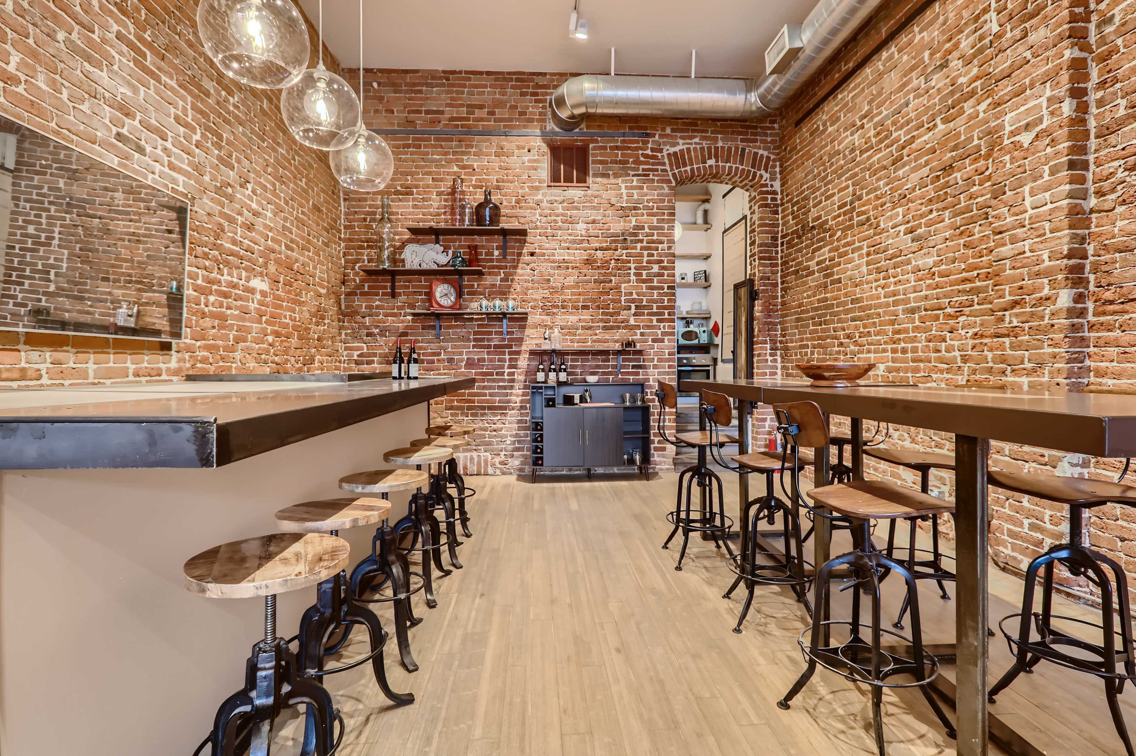 A rustic bar area with exposed brick walls, wooden stools, and a long countertop.