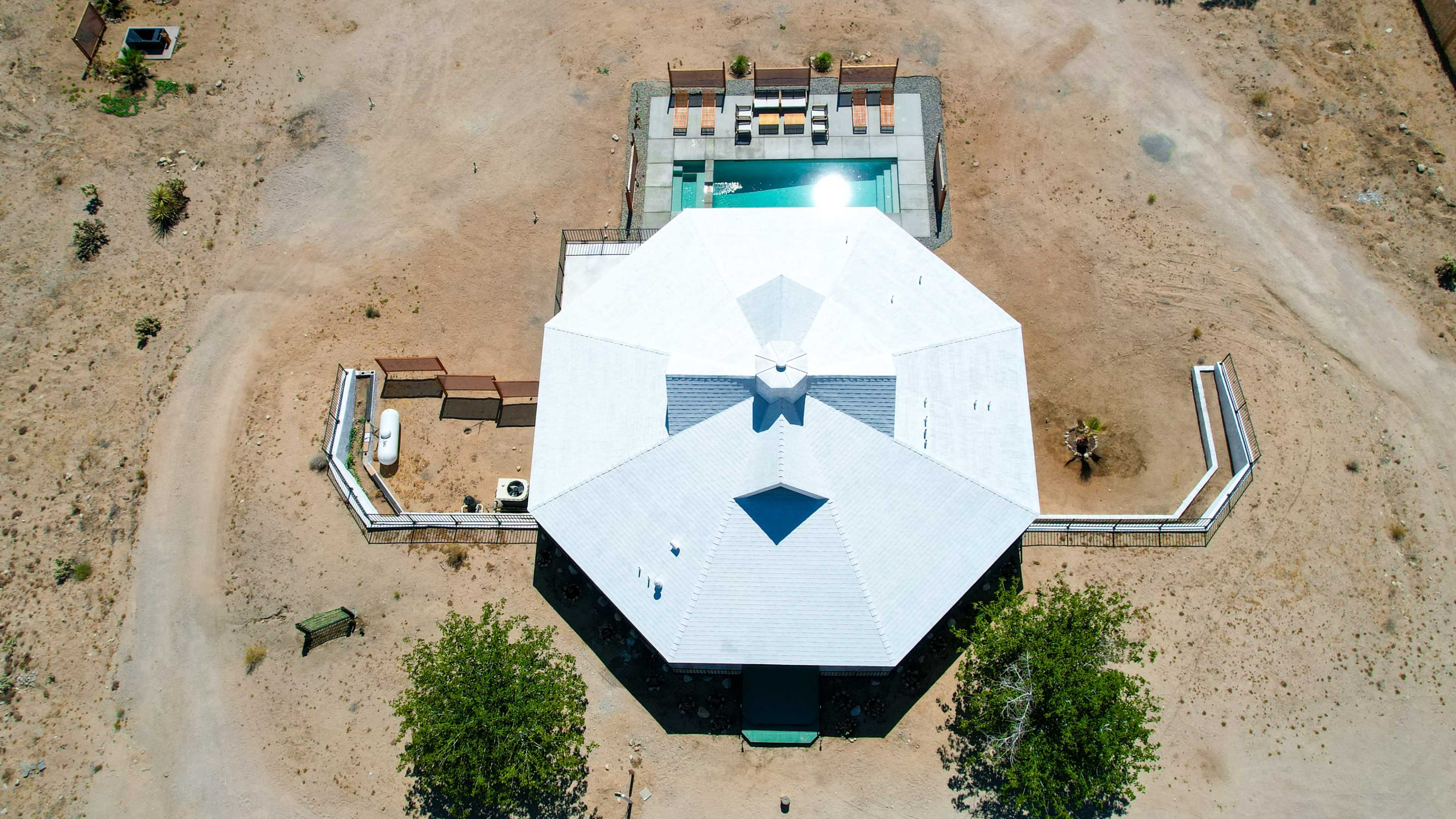 An octagonal house is situated in a barren landscape with a swimming pool and surrounding patio area visible at the rear.