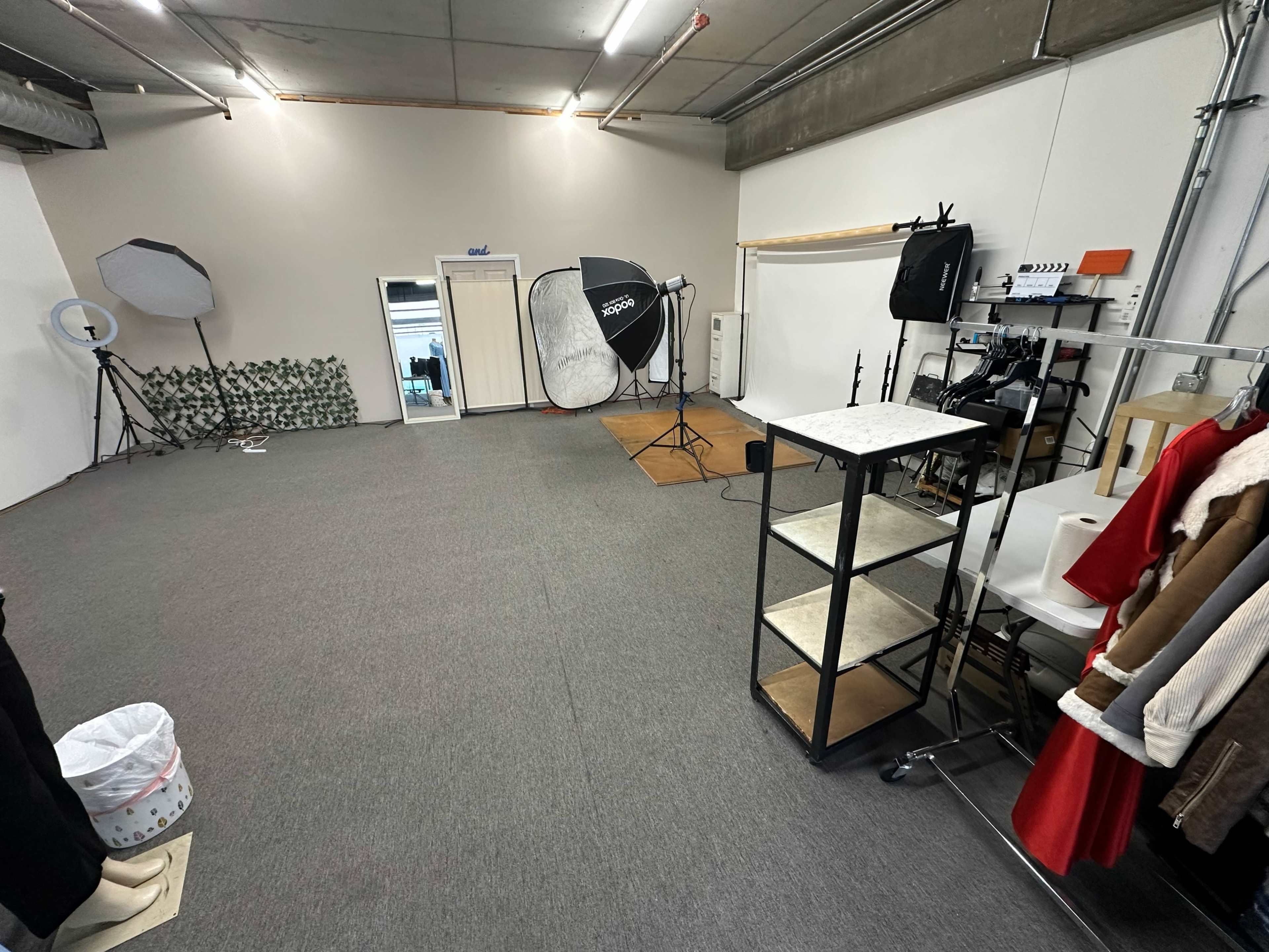 The image shows a spacious studio setup featuring photography equipment, a clothing rack, and a plain wall.