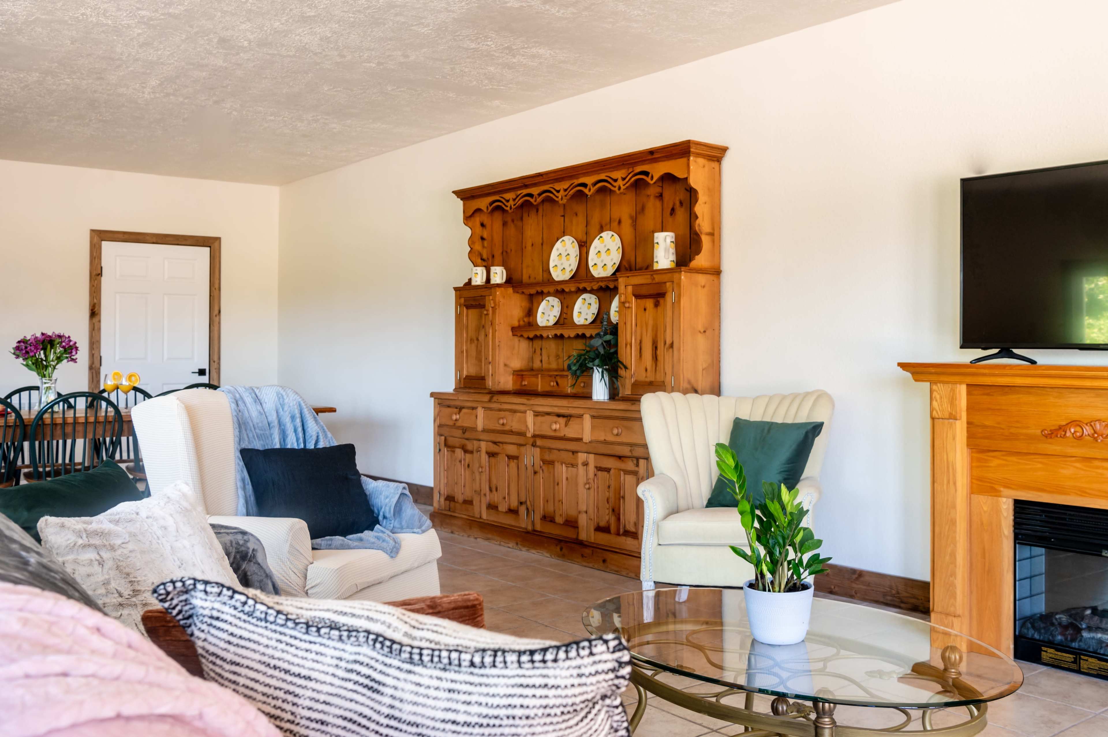 A living room with wooden furniture, including a cabinet and armchairs, a coffee table, and a television mounted on the wall.