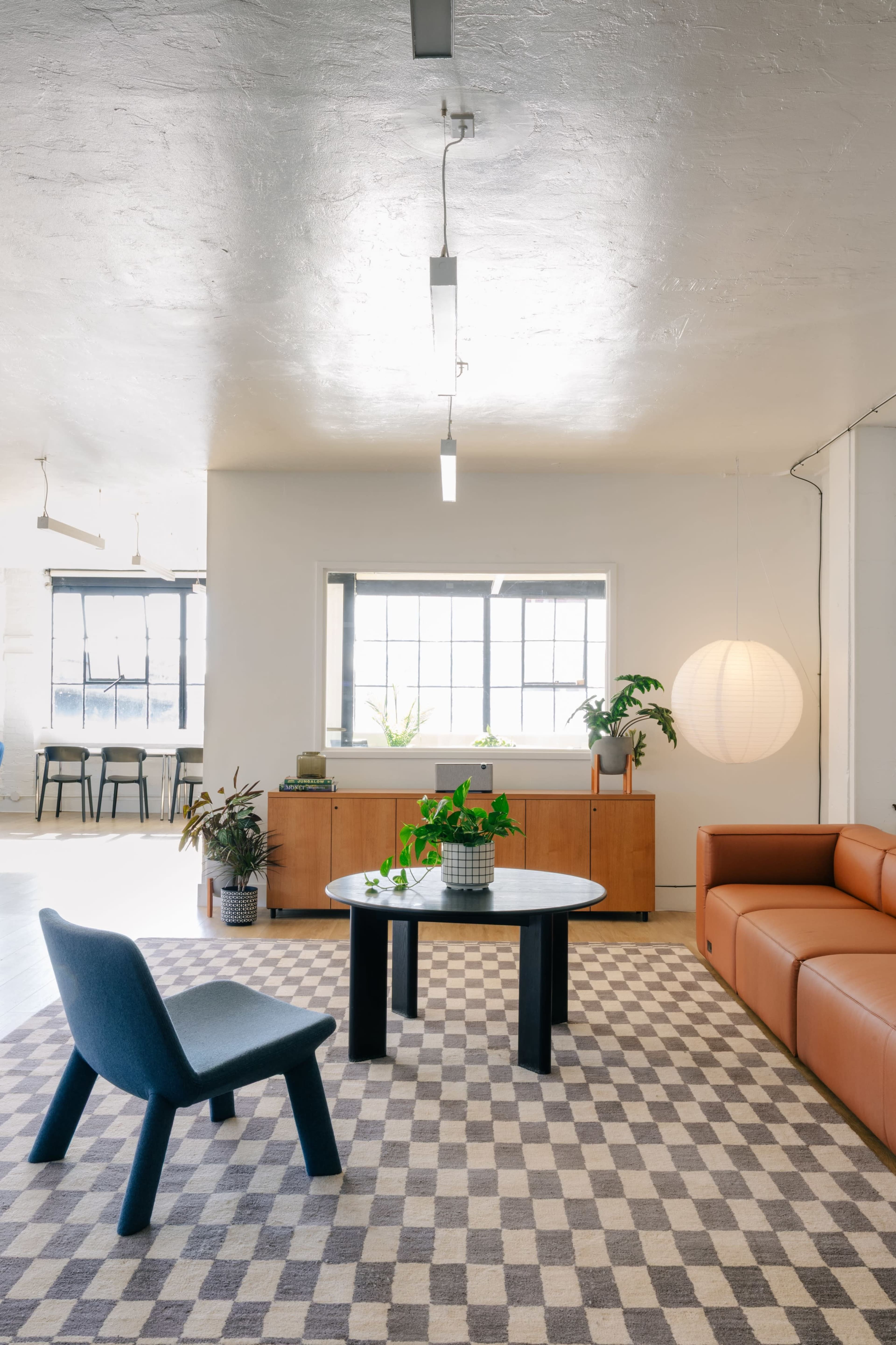 The image shows a modern living space featuring a leather sofa, a round coffee table, and a checkered rug, illuminated by overhead lights.
