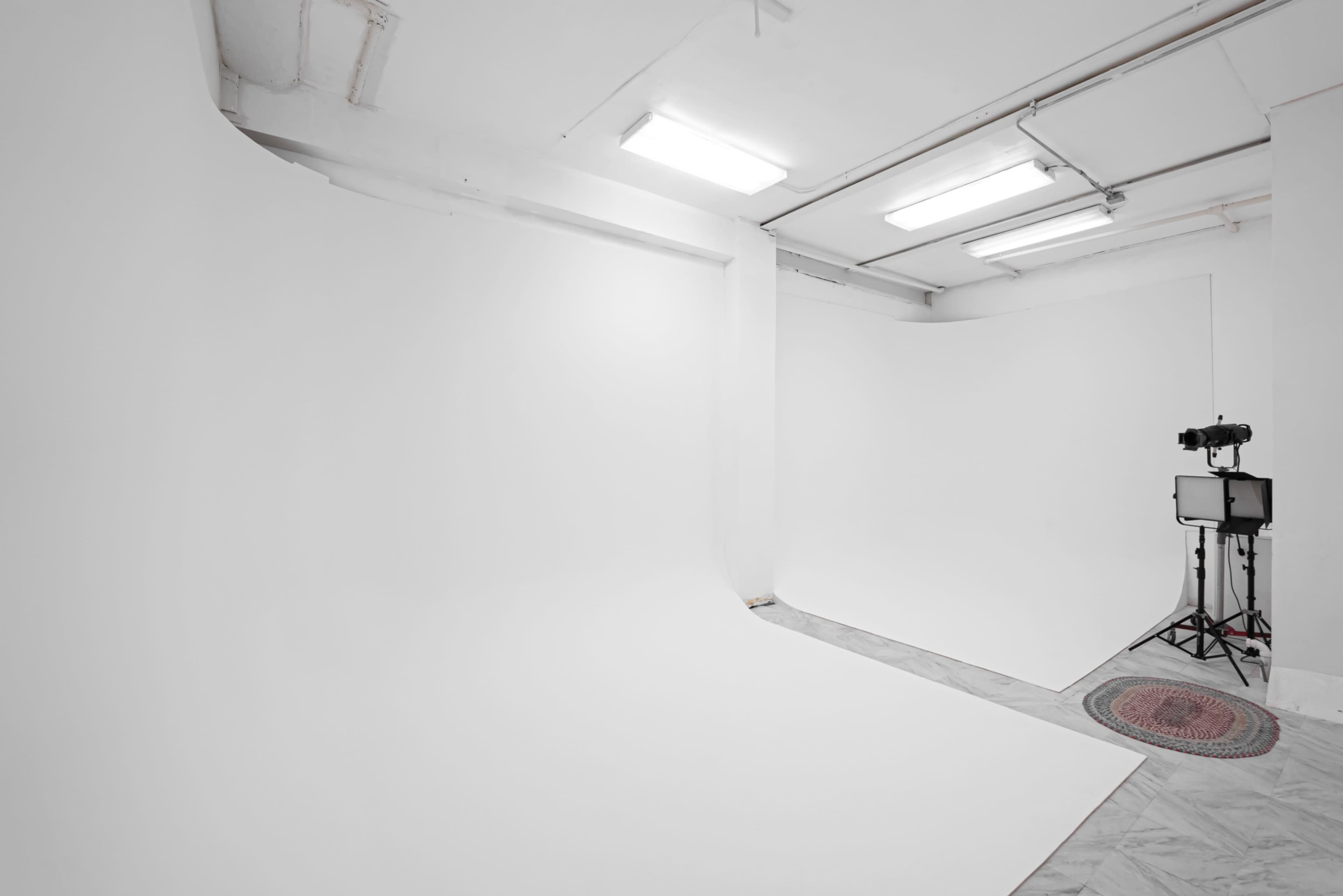 The image shows a spacious, well-lit photography studio with white walls and a seamless backdrop.
