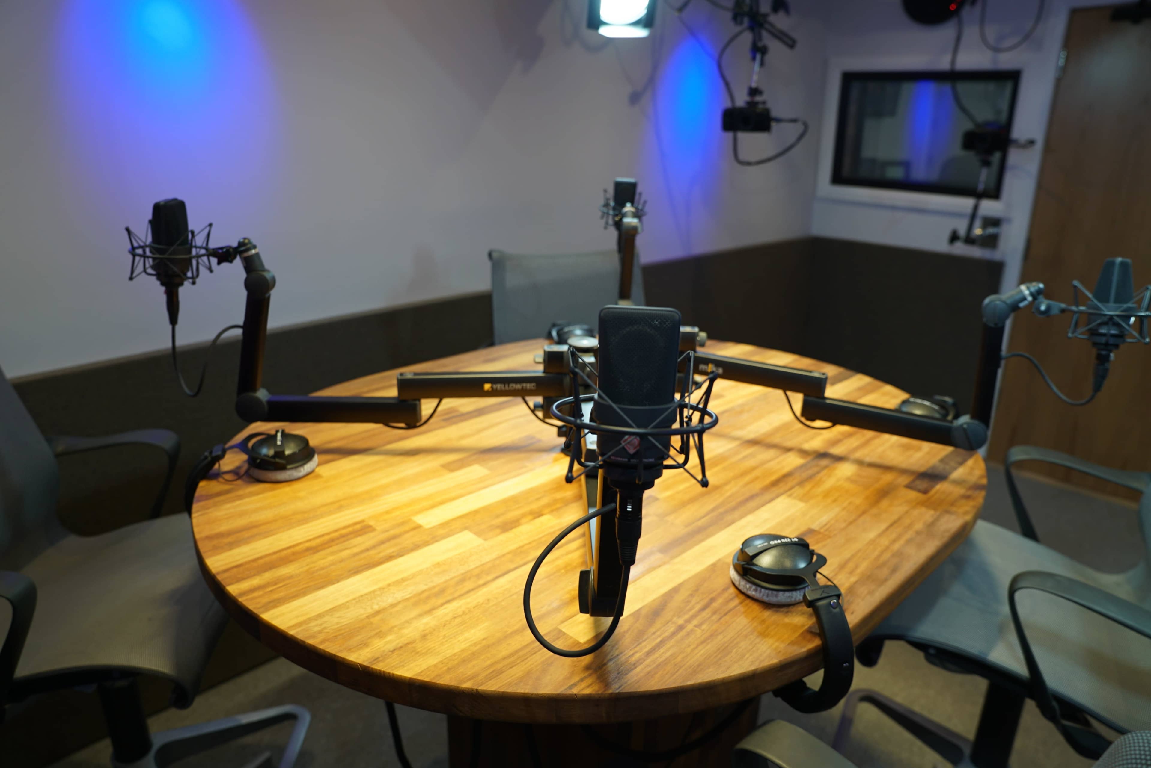 A circular wooden table with multiple microphones and headphones set up in a recording studio.