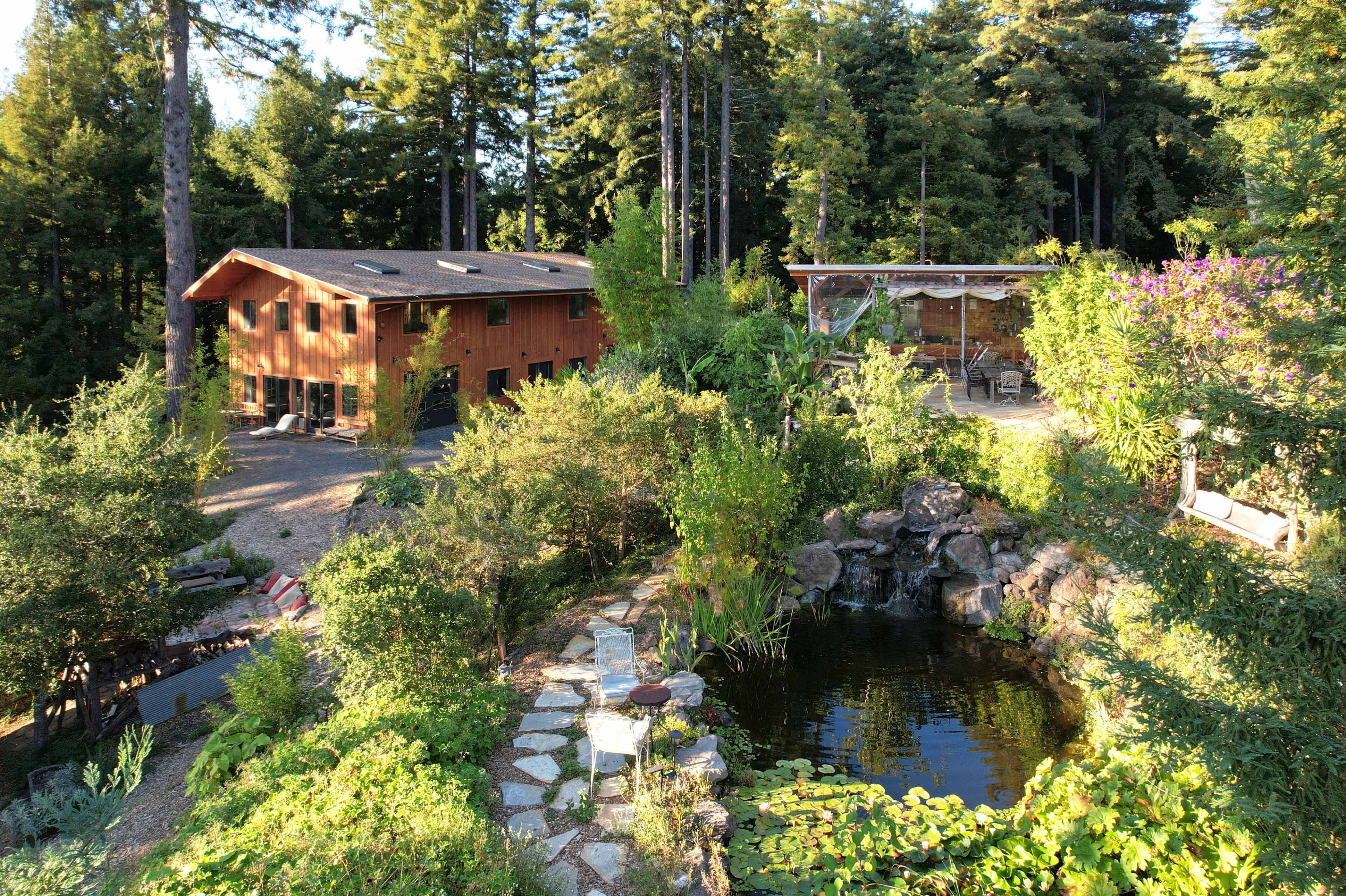 A wooden building next to a pond surrounded by lush greenery and tall trees.