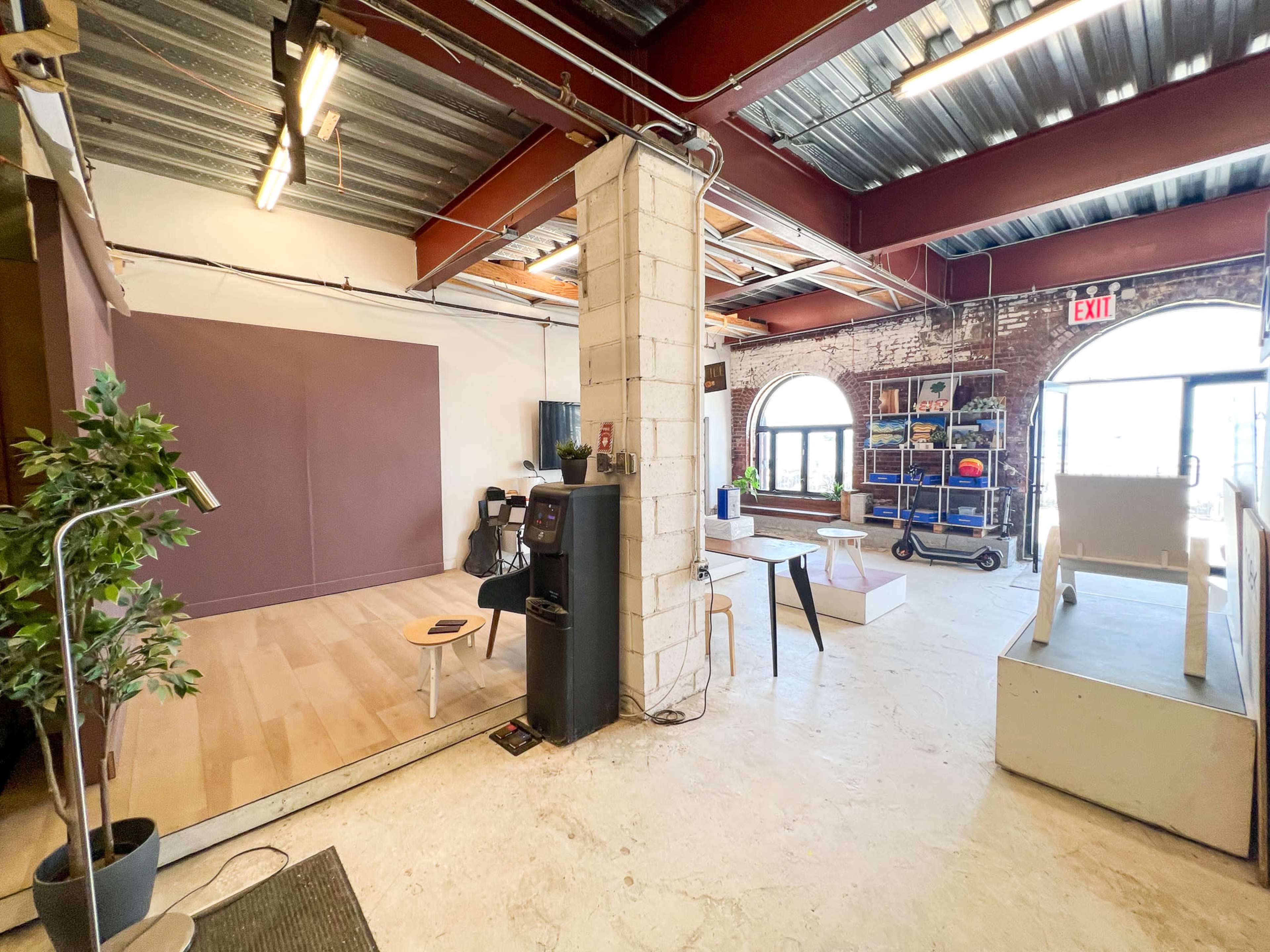 The image shows an industrial-style open space with wooden flooring, a purple backdrop on one side, and various furniture items scattered throughout.