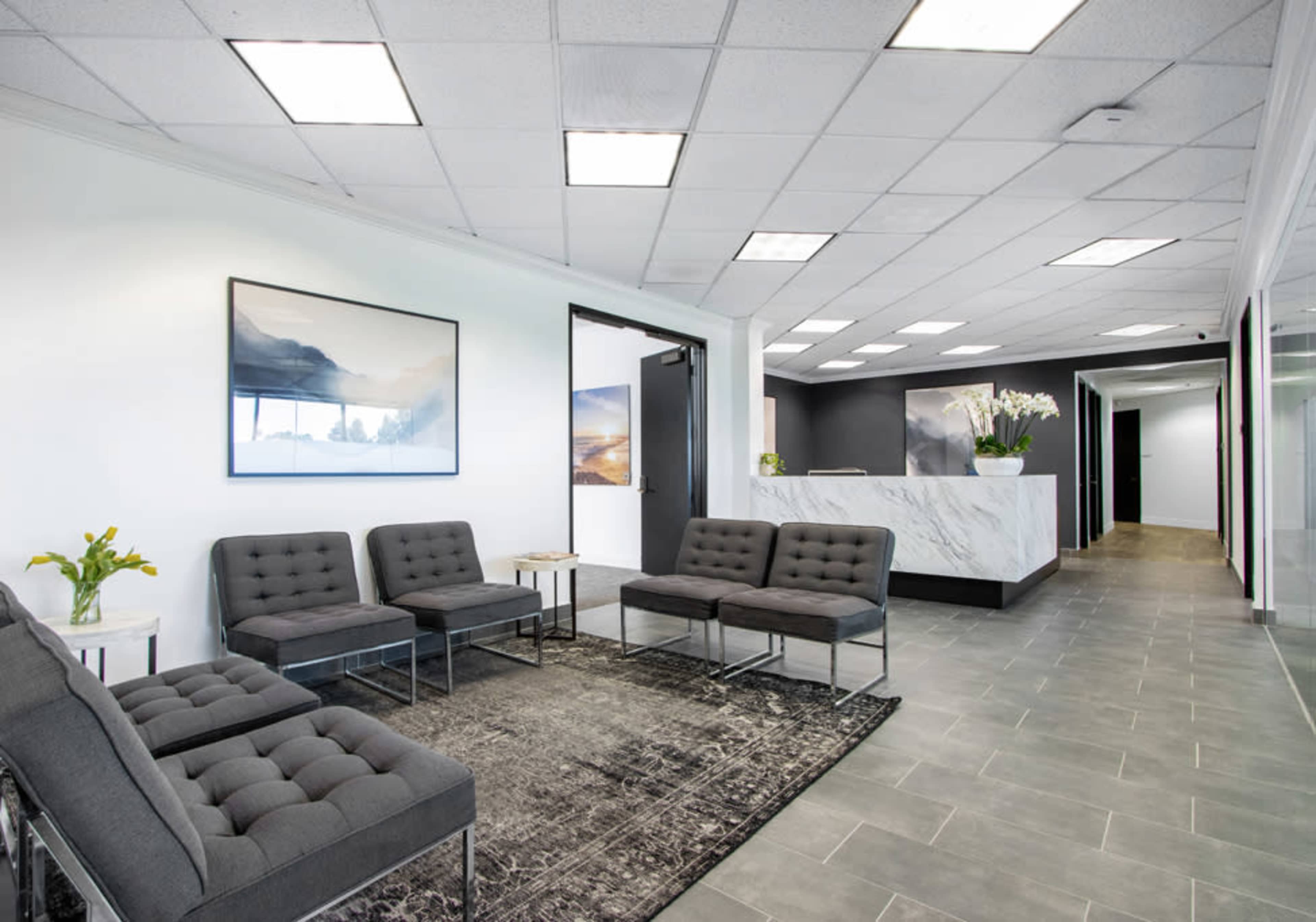 The image shows a modern reception area with gray seating, a marble front desk, and artwork on the walls.
