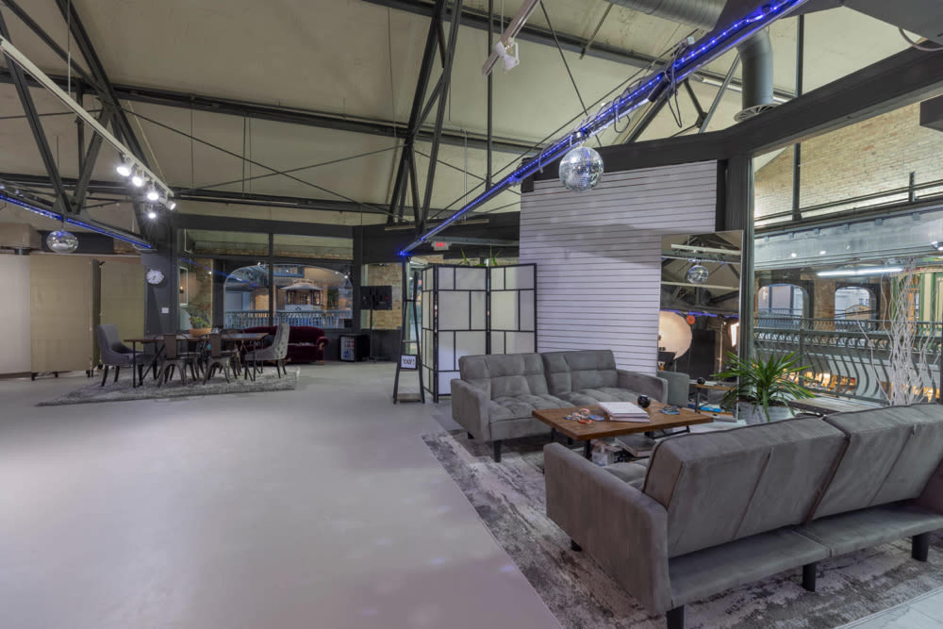 A modern open space with gray sofas, a dining area with a table, and large windows allowing natural light in.