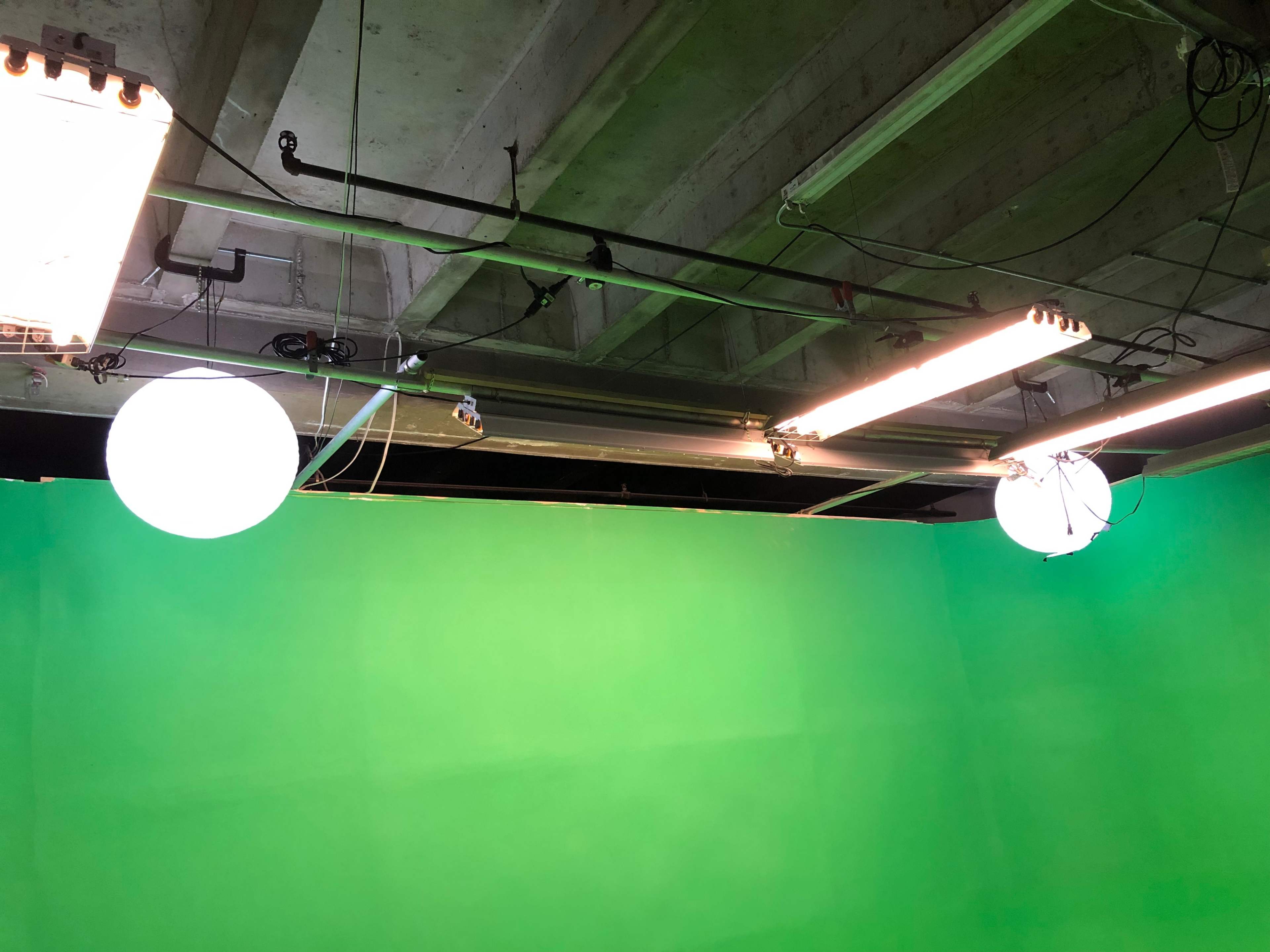 A studio space with green backdrop and overhead lighting fixtures.