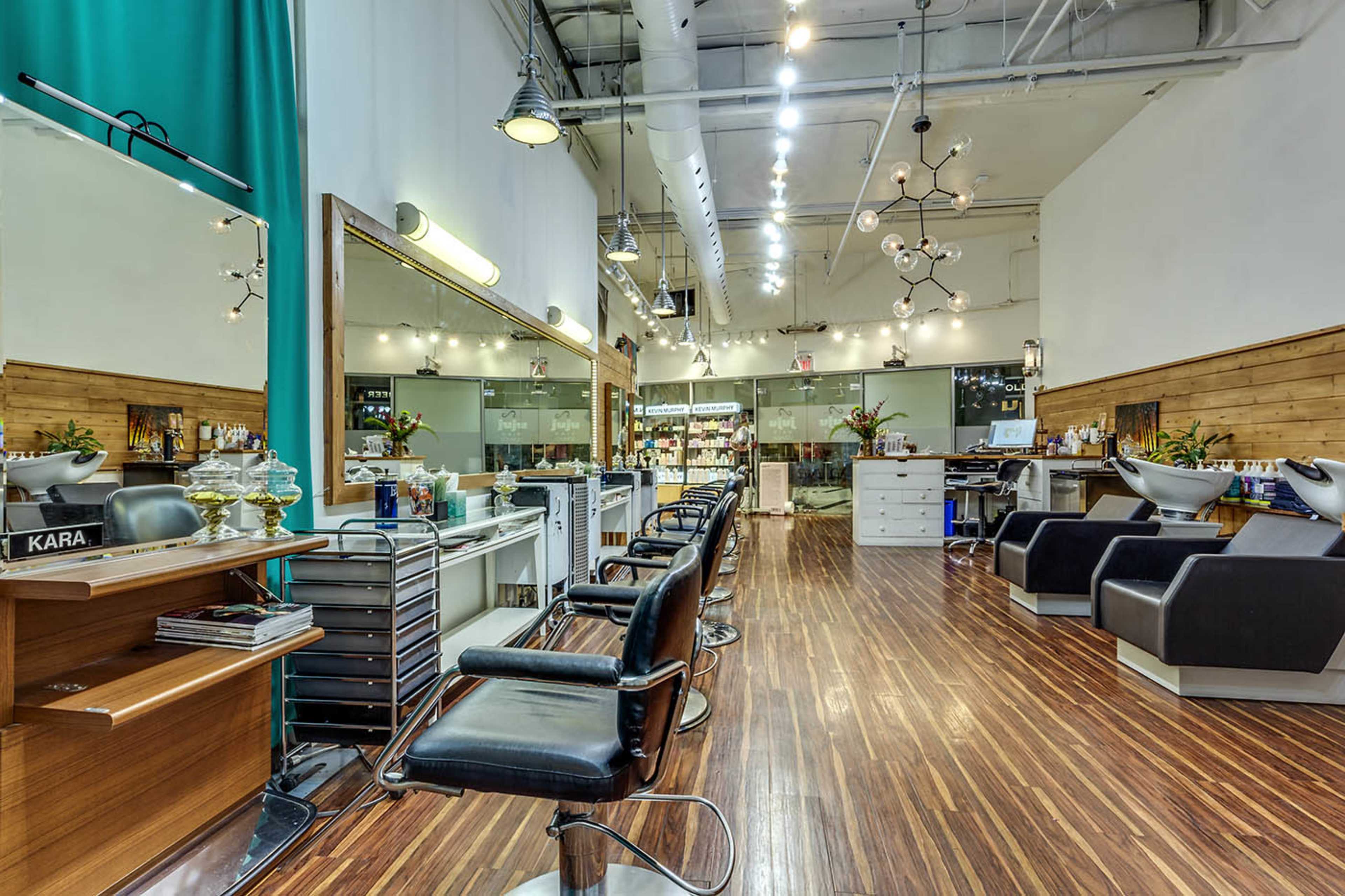 A hair salon interior features multiple styling stations with chairs, a mirror, and wash basins, all set in a spacious, well-lit environment.