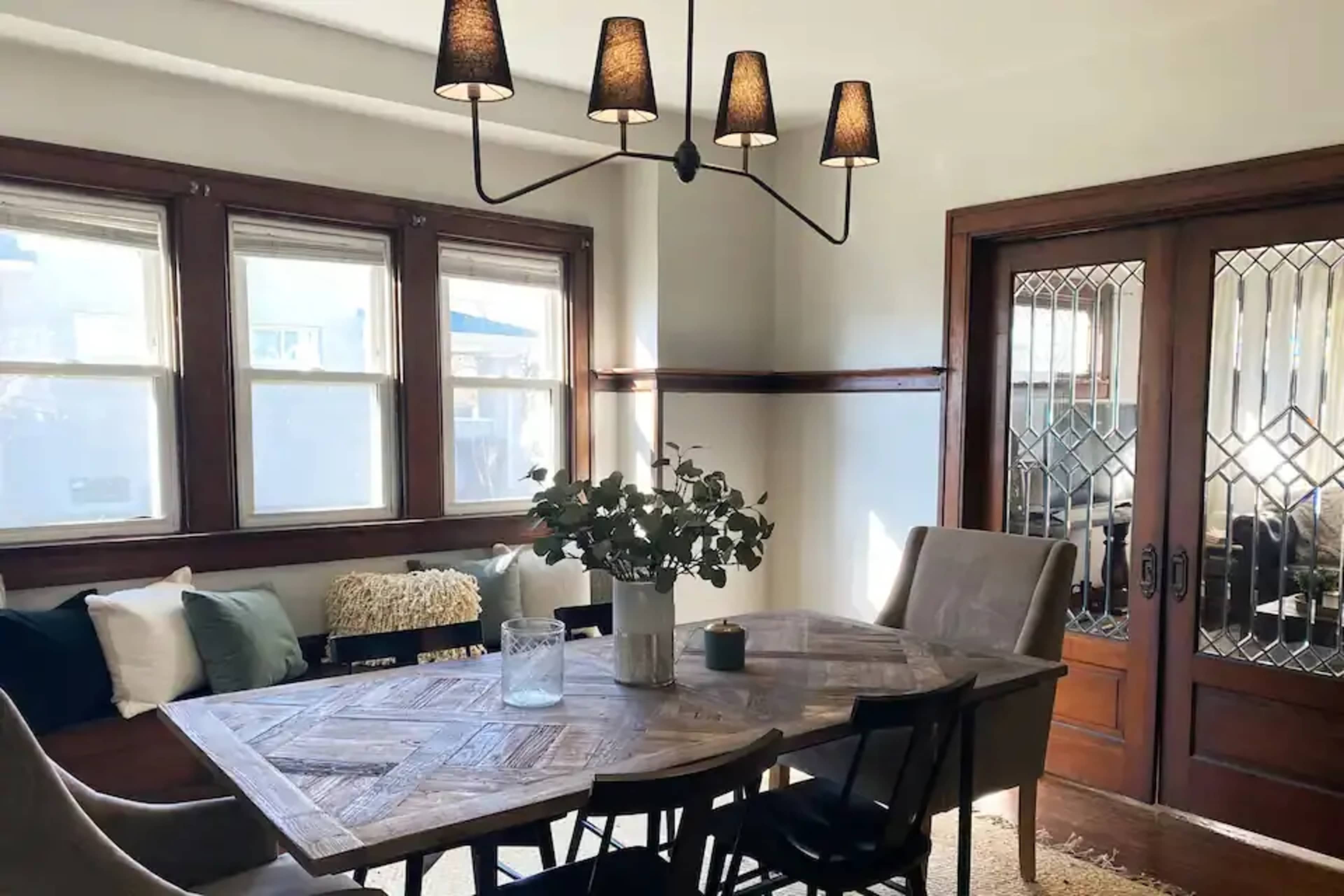 A dining area features a wooden table surrounded by chairs, with a light fixture above and glass-paned doors leading outside.