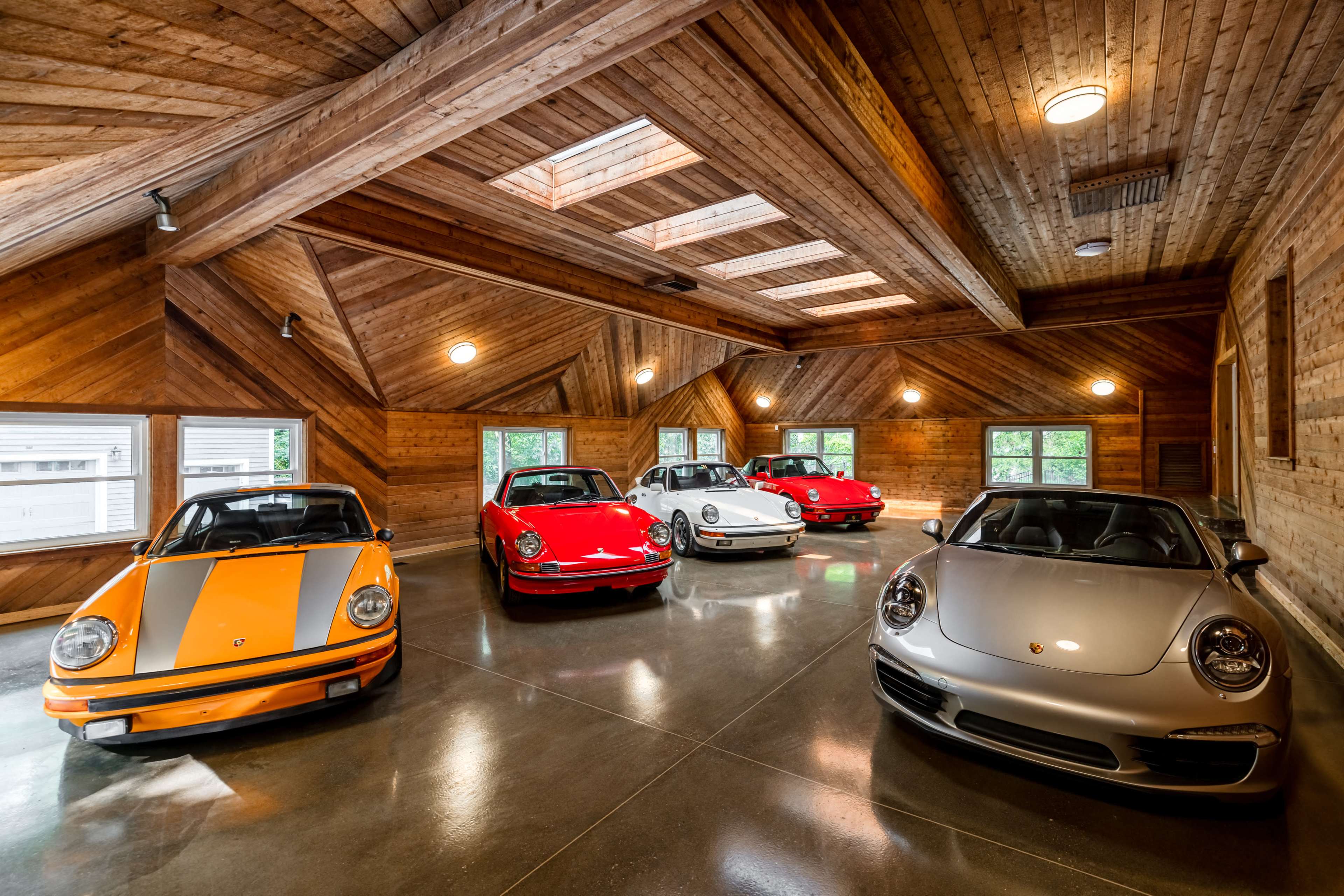 A garage with five classic and modern Porsche cars arranged in a wooden-paneled space with skylights.