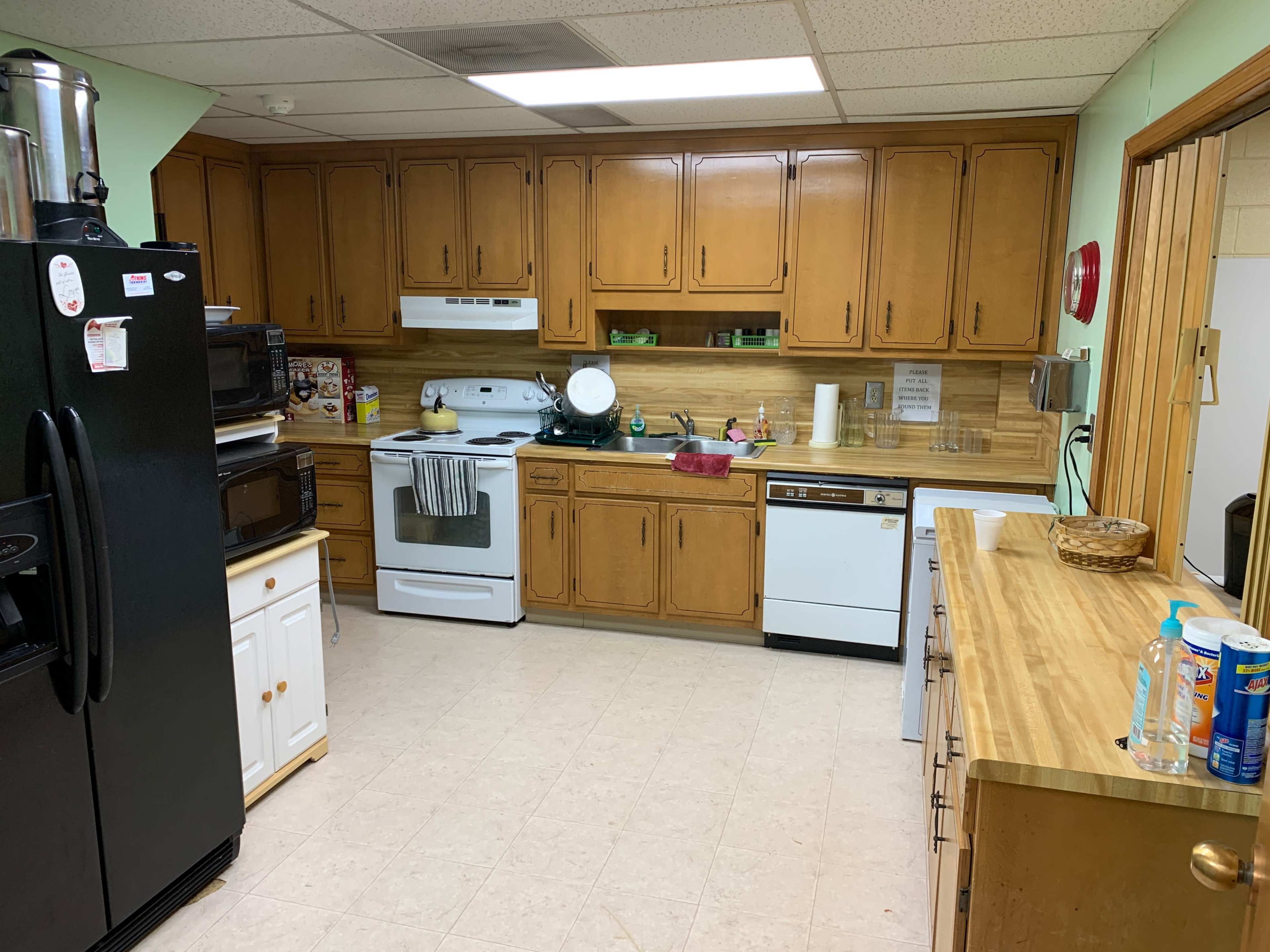 A kitchen with wooden cabinets, a white stove and dishwasher, a black refrigerator, and a countertop with various kitchen items.