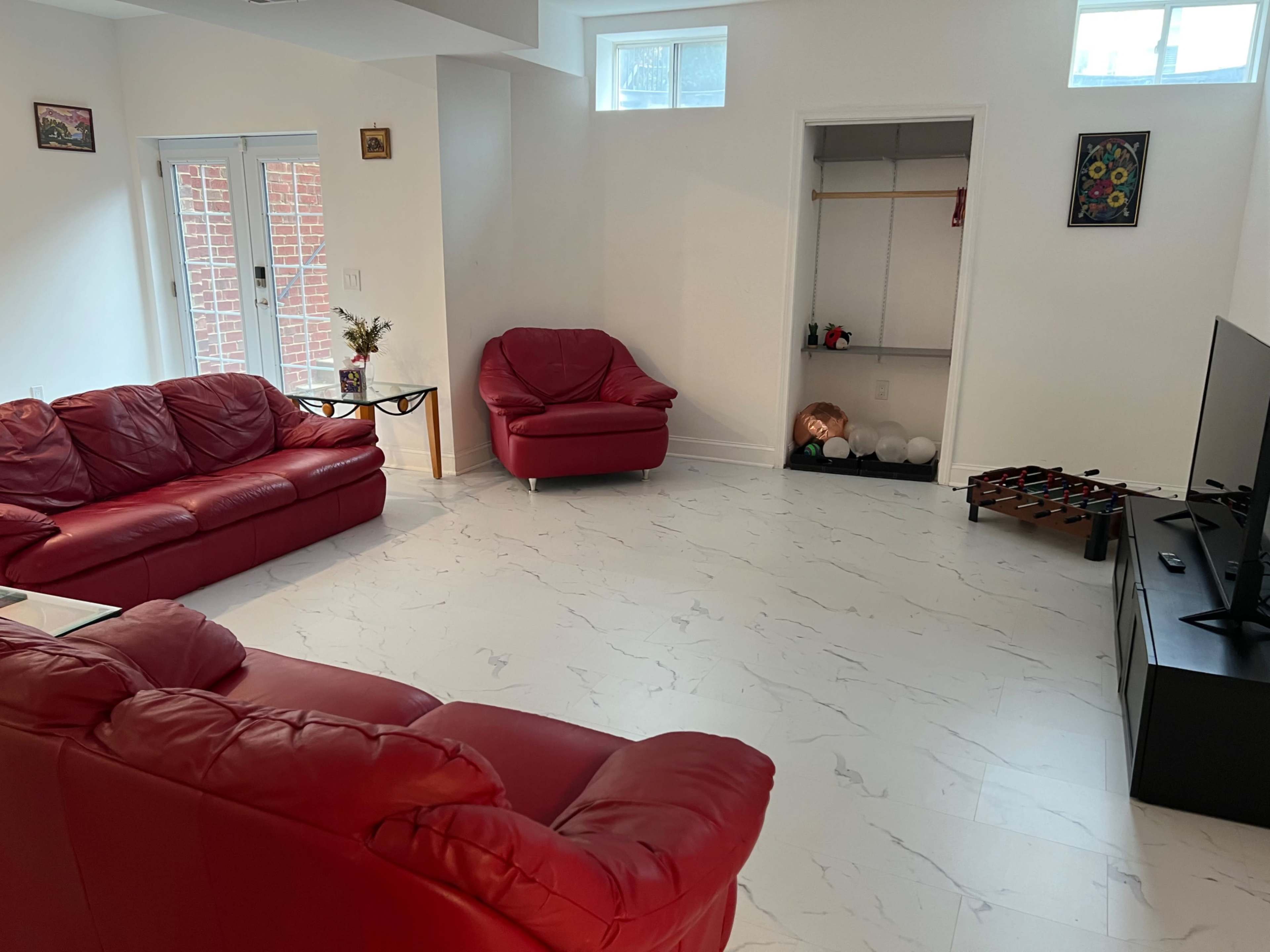 The room features red leather furniture arranged around a television on a black stand and has a minimalistic design with white marble flooring.