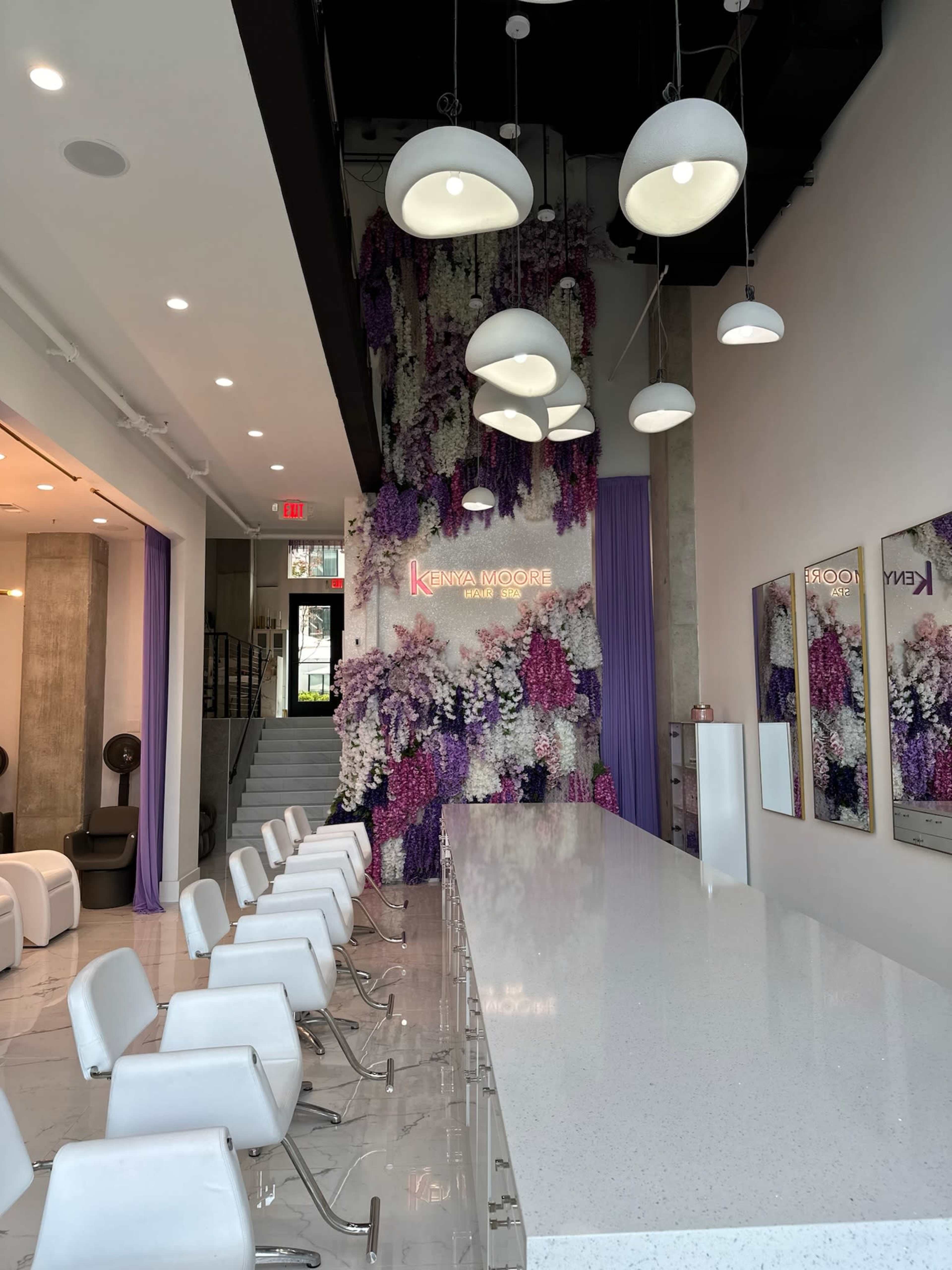 The interior of a modern salon features a long white counter with bar seating and a wall adorned with vibrant floral arrangements.