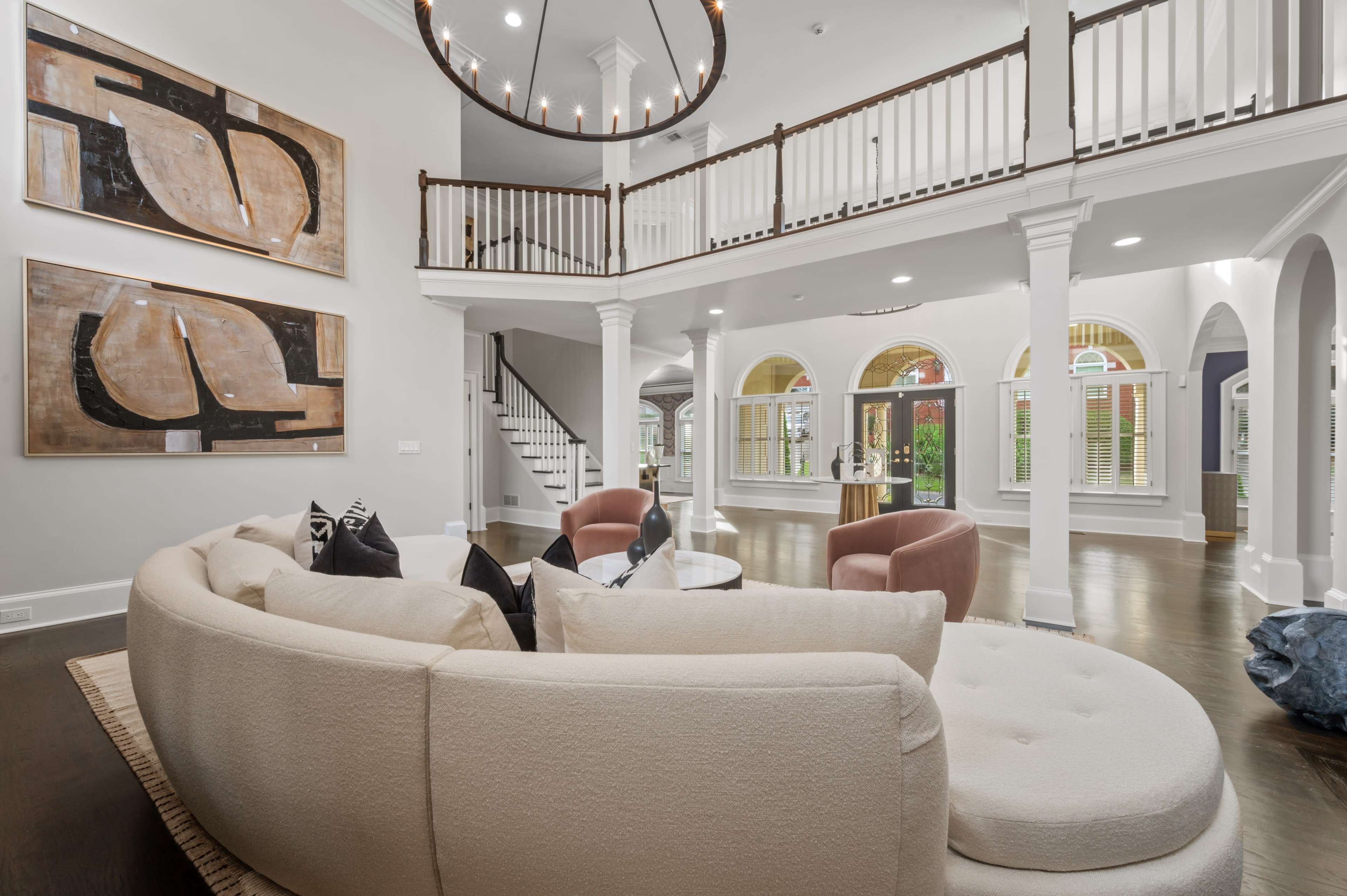 A spacious living room featuring a large curved sofa, contemporary art on the walls, and a staircase leading to an upper level.