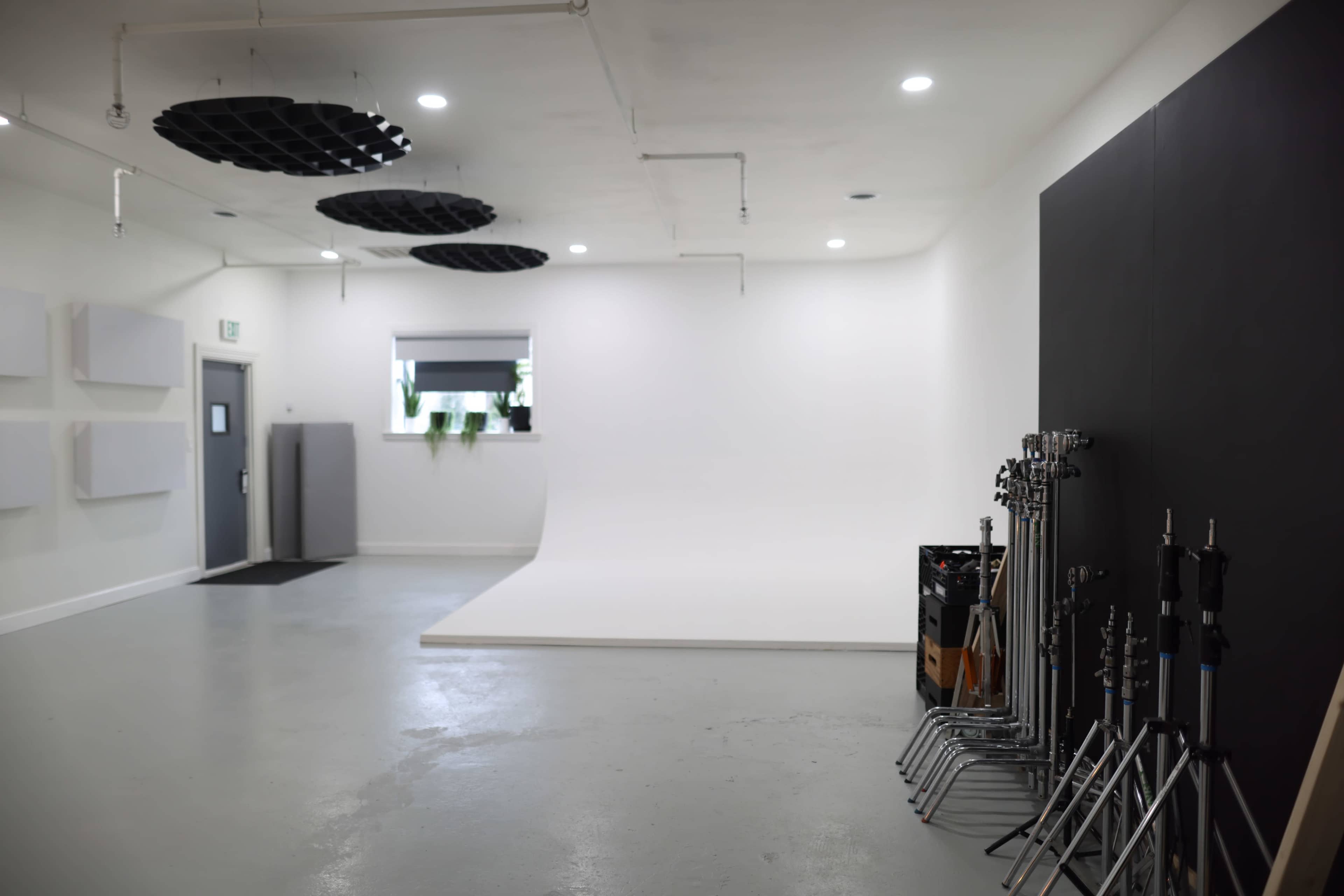 A spacious, well-lit studio with a white backdrop, a gray door, and various equipment stands arranged along one side.