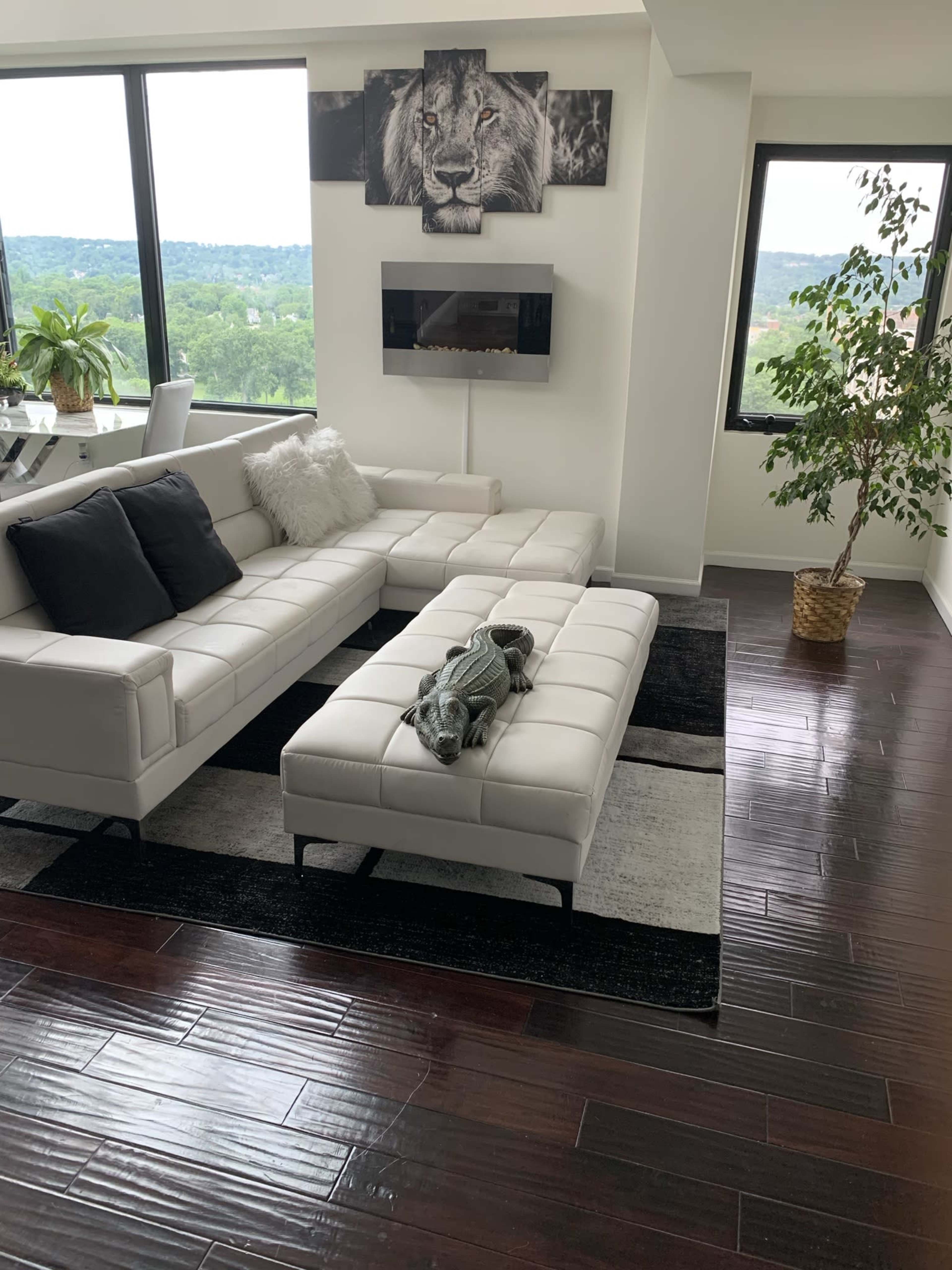A modern living room with a white sectional sofa, a decorative lion wall art, and large windows overlooking greenery.