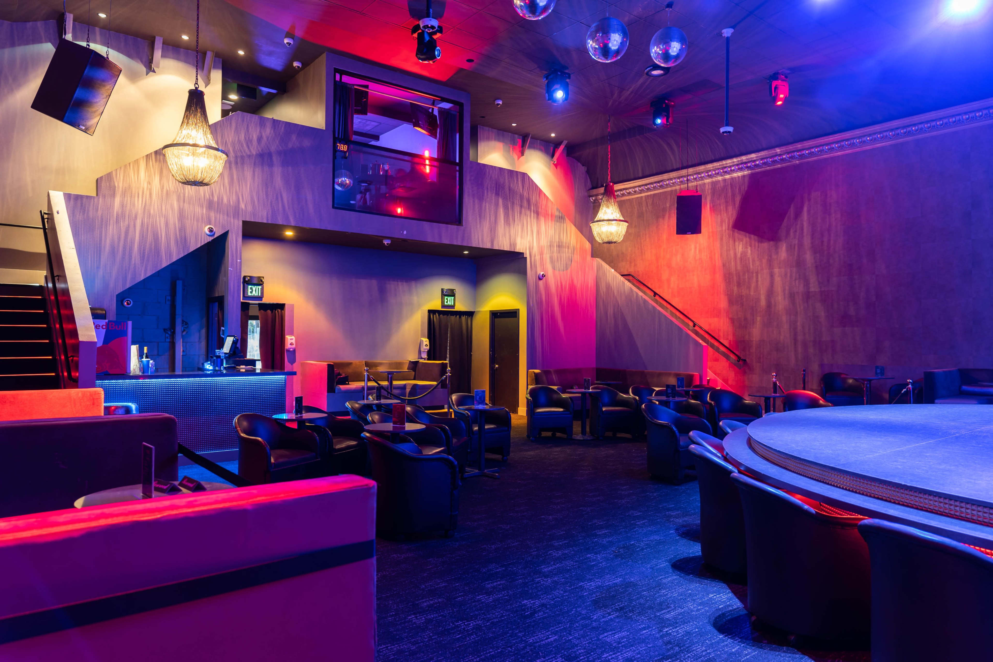A dimly lit lounge area with seating, a stage, and decorative lighting fixtures.