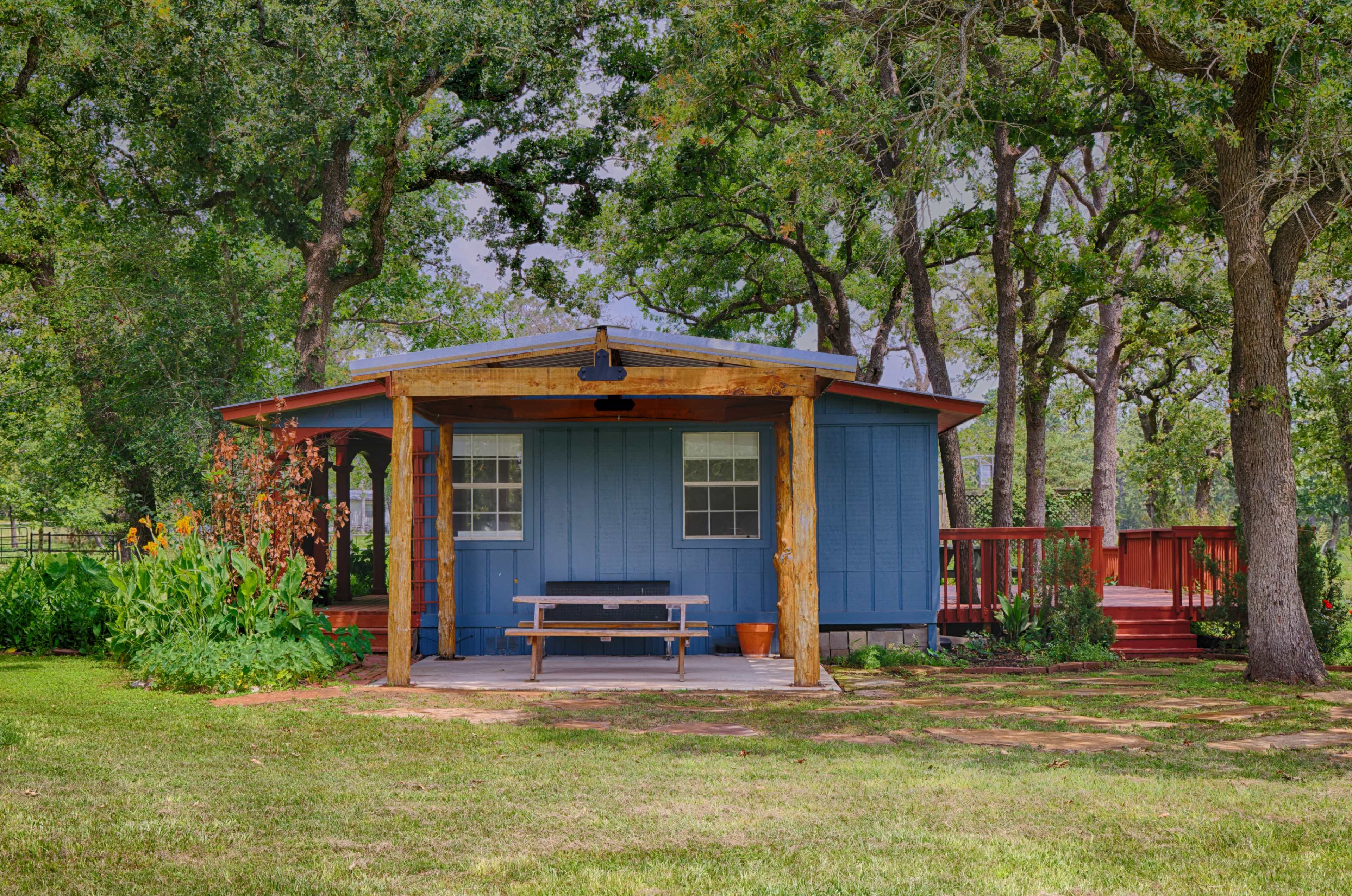 A blue wooden cabin with a covered porch is nestled among green trees and grass.