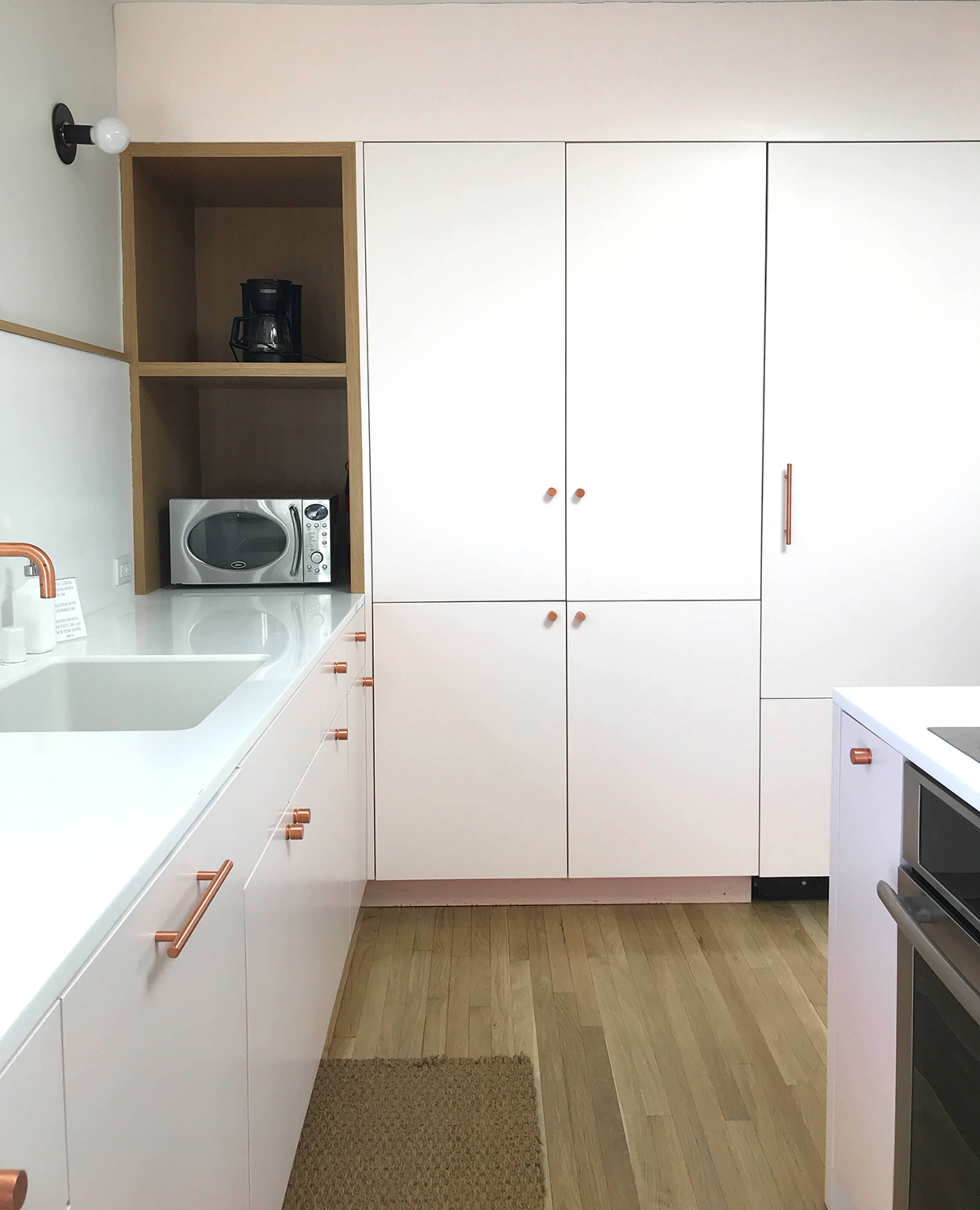 The image shows a modern kitchen with white cabinets, a built-in microwave, and a coffee maker on a shelf.