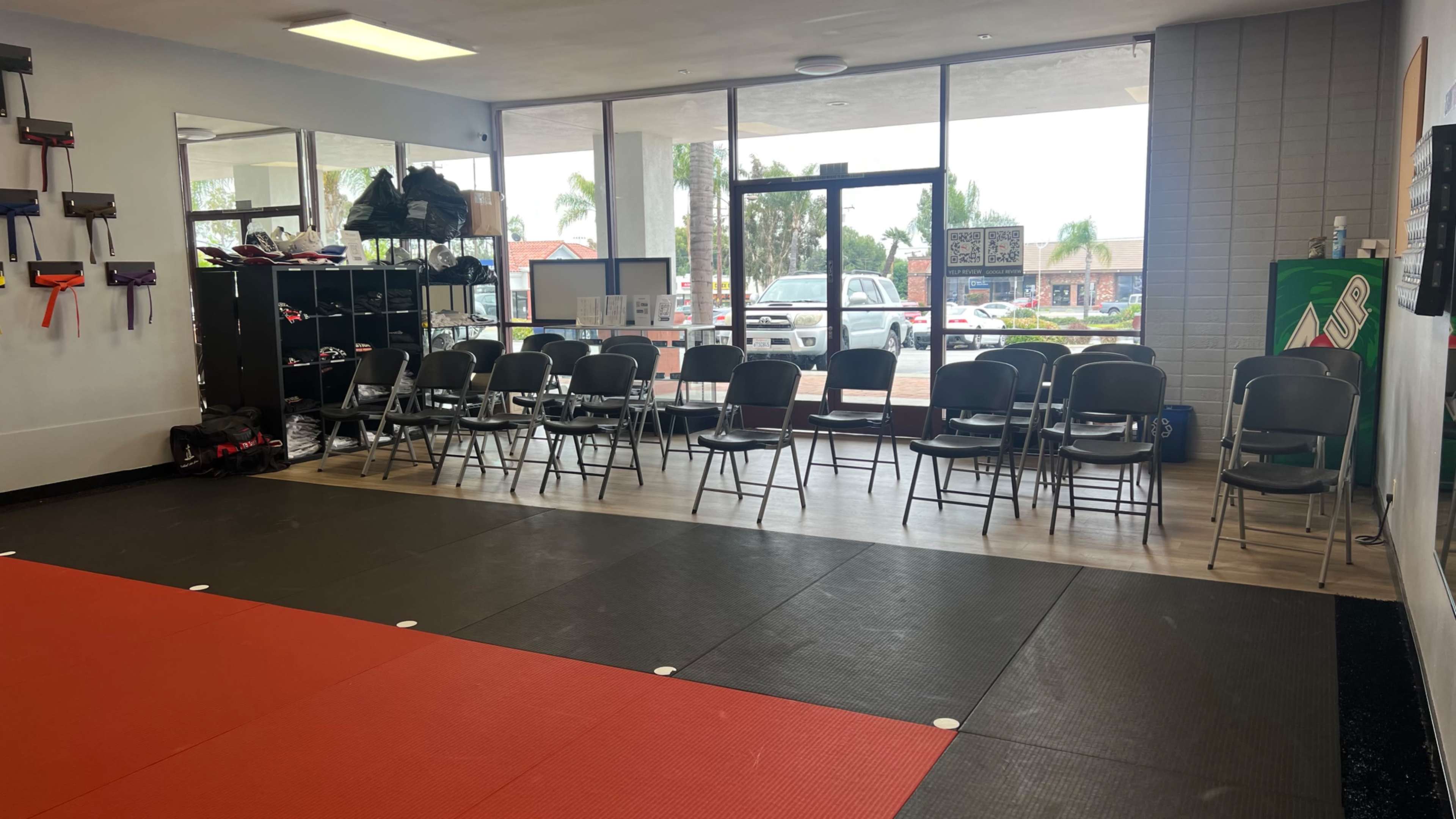 An interior space with a red and black padded floor, a row of black chairs facing a large window, and shelves holding various equipment.