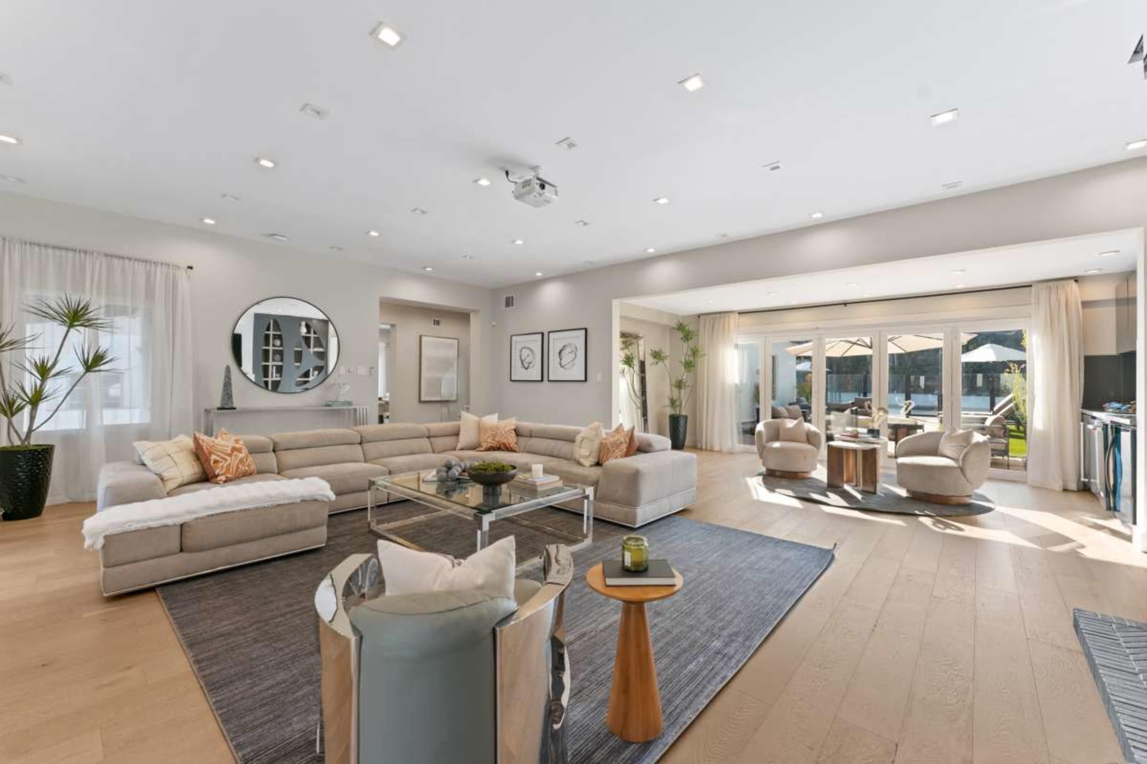 The spacious living room features a large sectional sofa, a glass coffee table, and a view of an outdoor patio through expansive sliding glass doors.