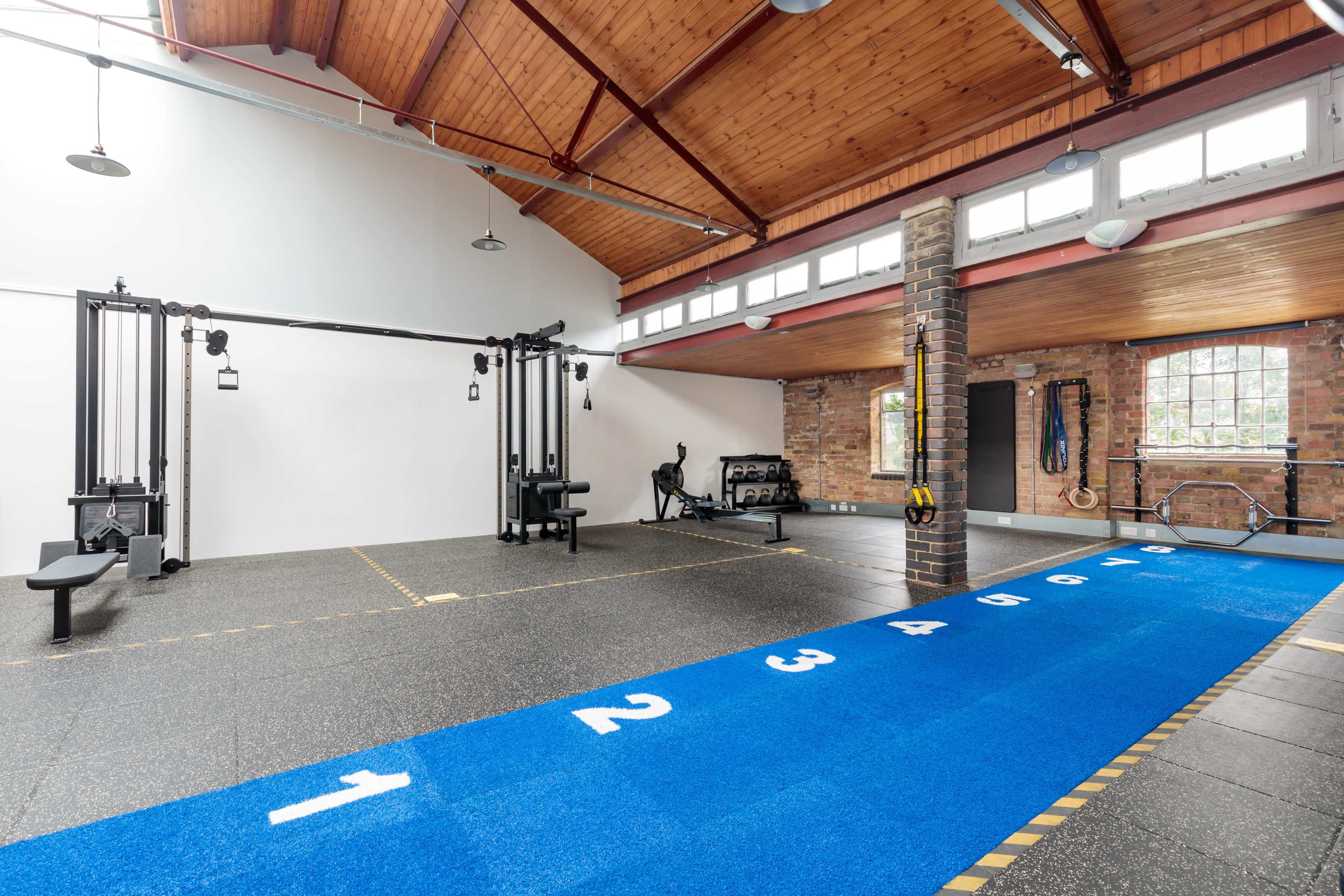 A modern gym interior featuring exercise equipment, a blue numbered track, and a high wooden ceiling.