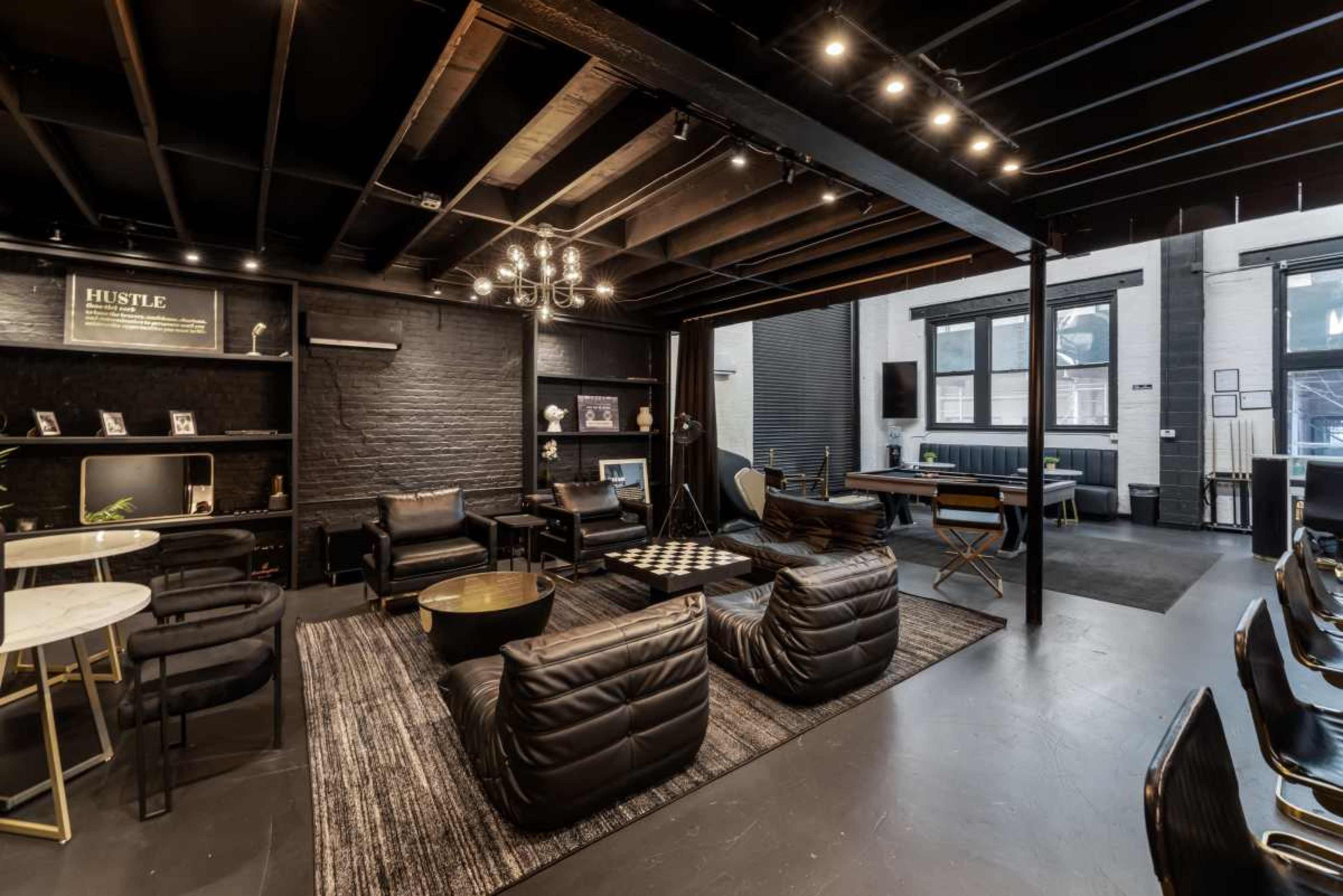 The image shows a modern lounge area featuring black furniture, a chessboard, a bar setup, and exposed wooden beams on the ceiling.