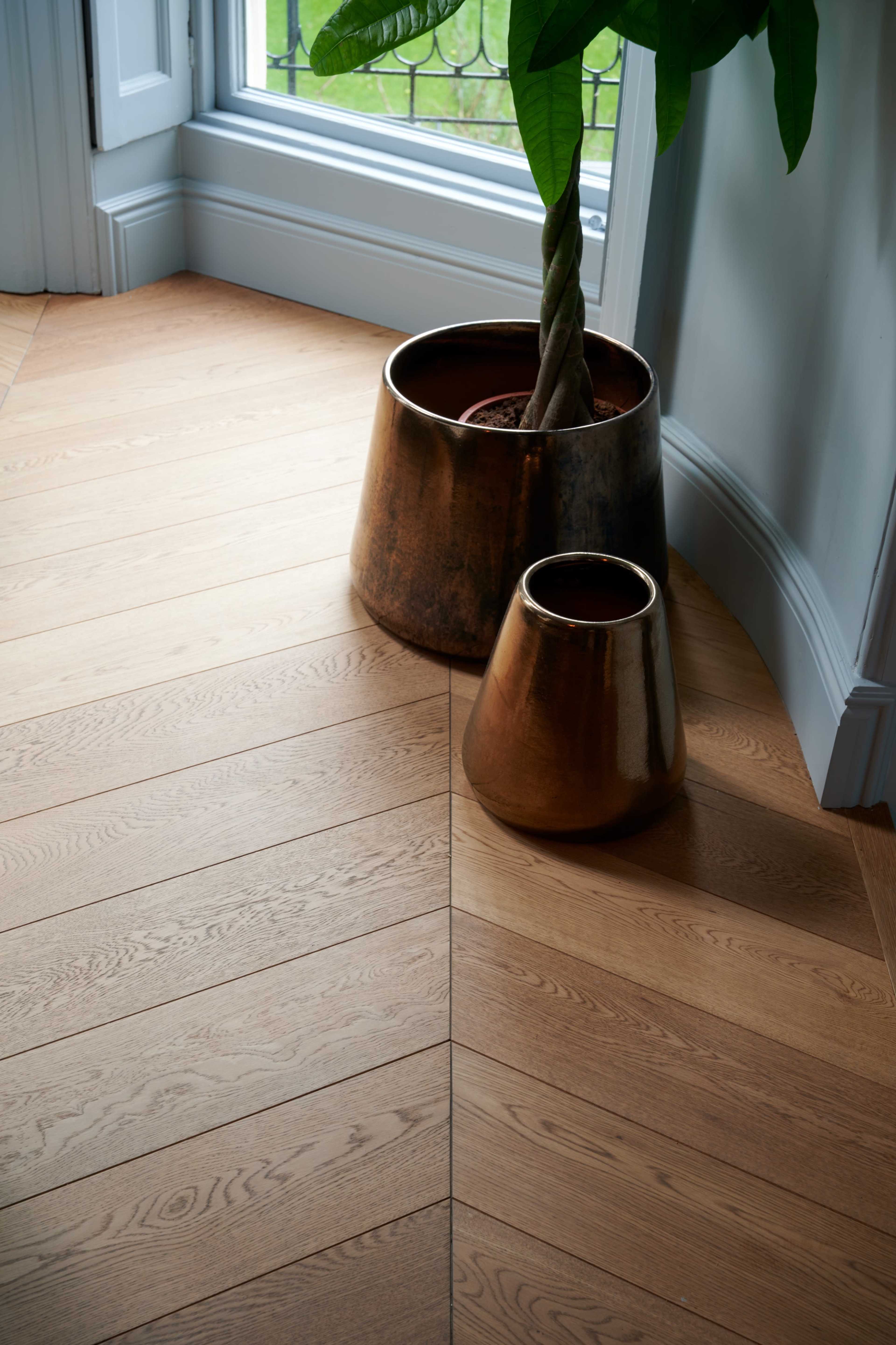 A large and a small metal planter are positioned on a wooden floor, near a window.