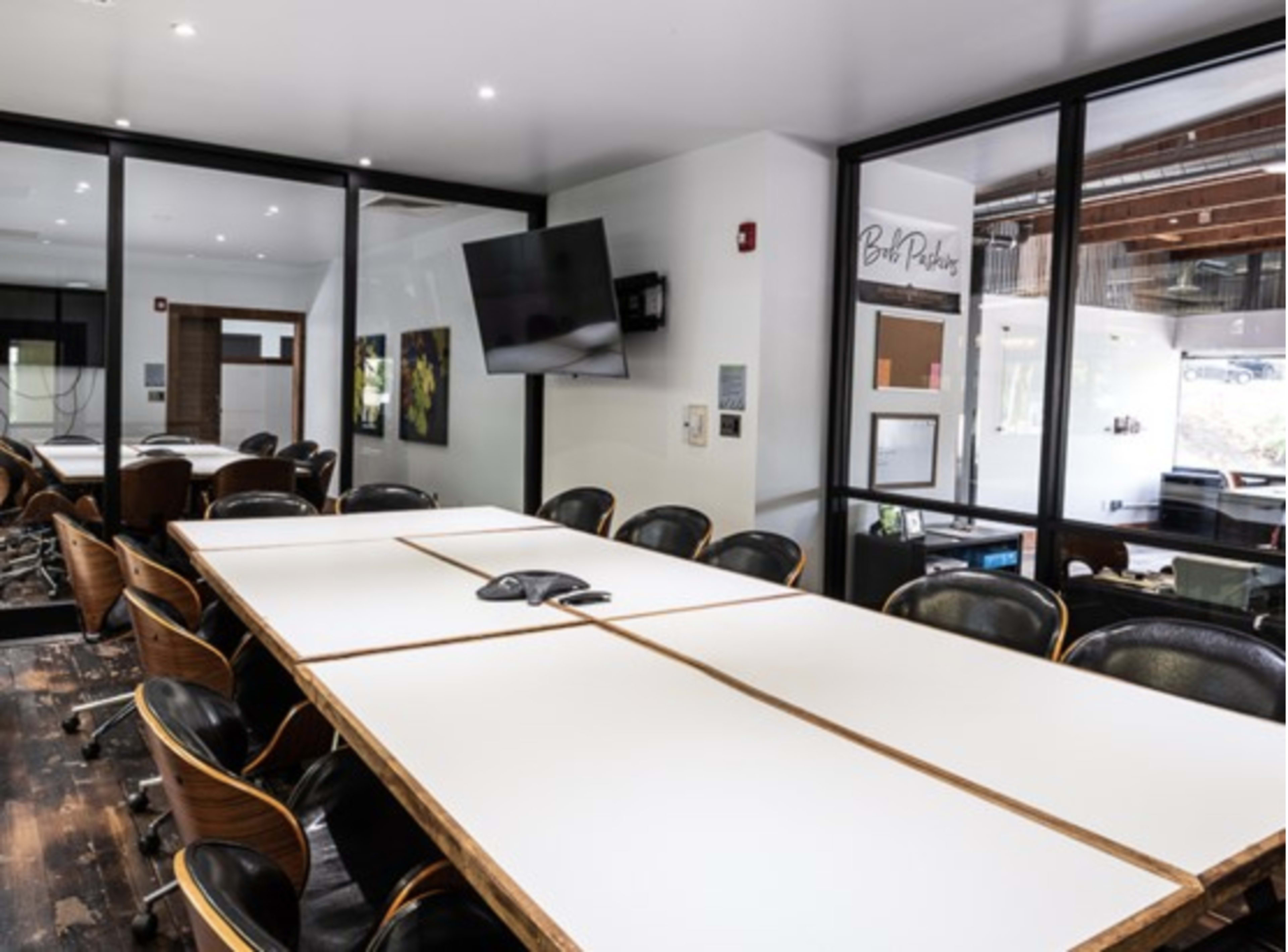 A modern conference room with a long wooden table surrounded by stylish black chairs and a large wall-mounted screen.