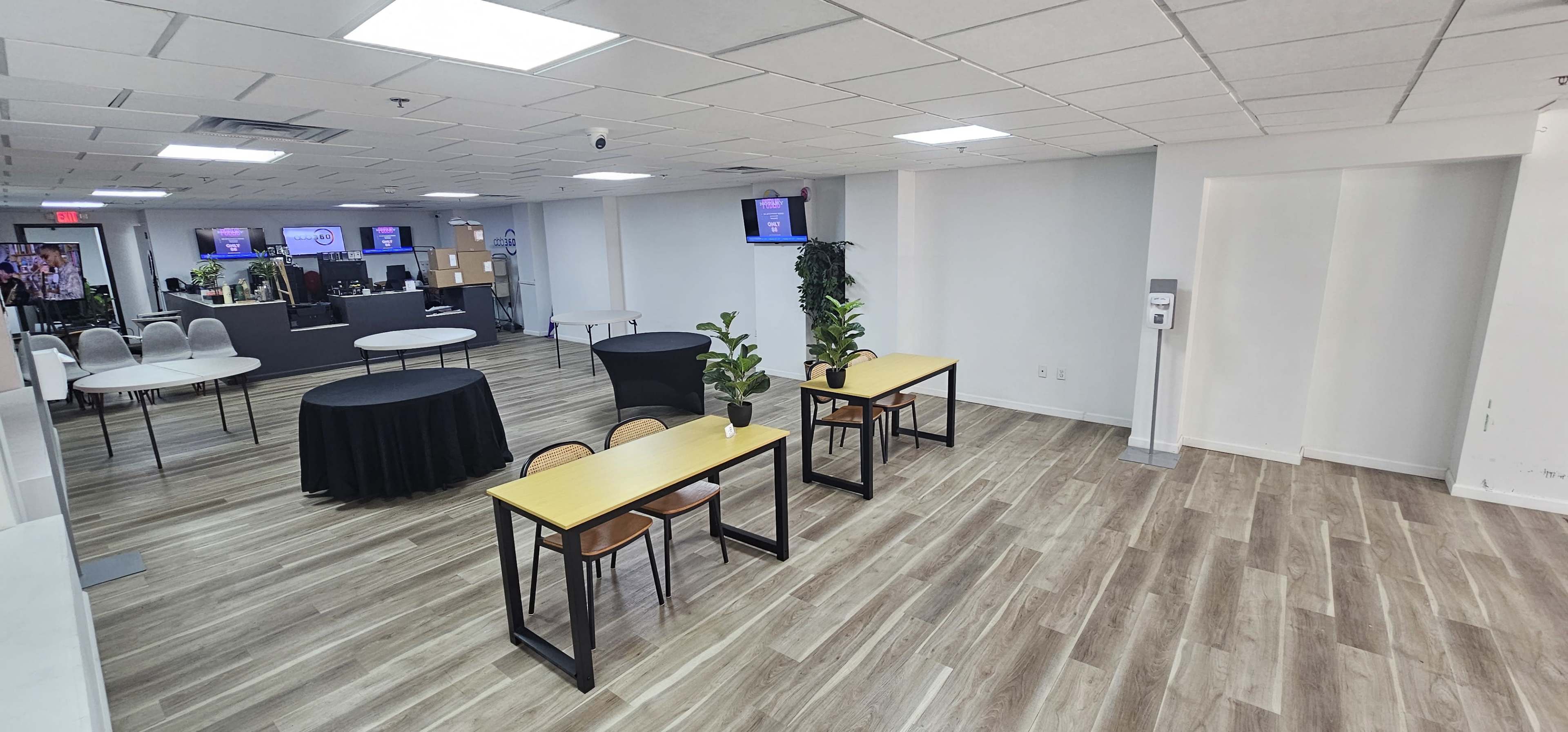 The image shows an office space with two tables and chairs arranged on one side, while a reception area is visible in the background.