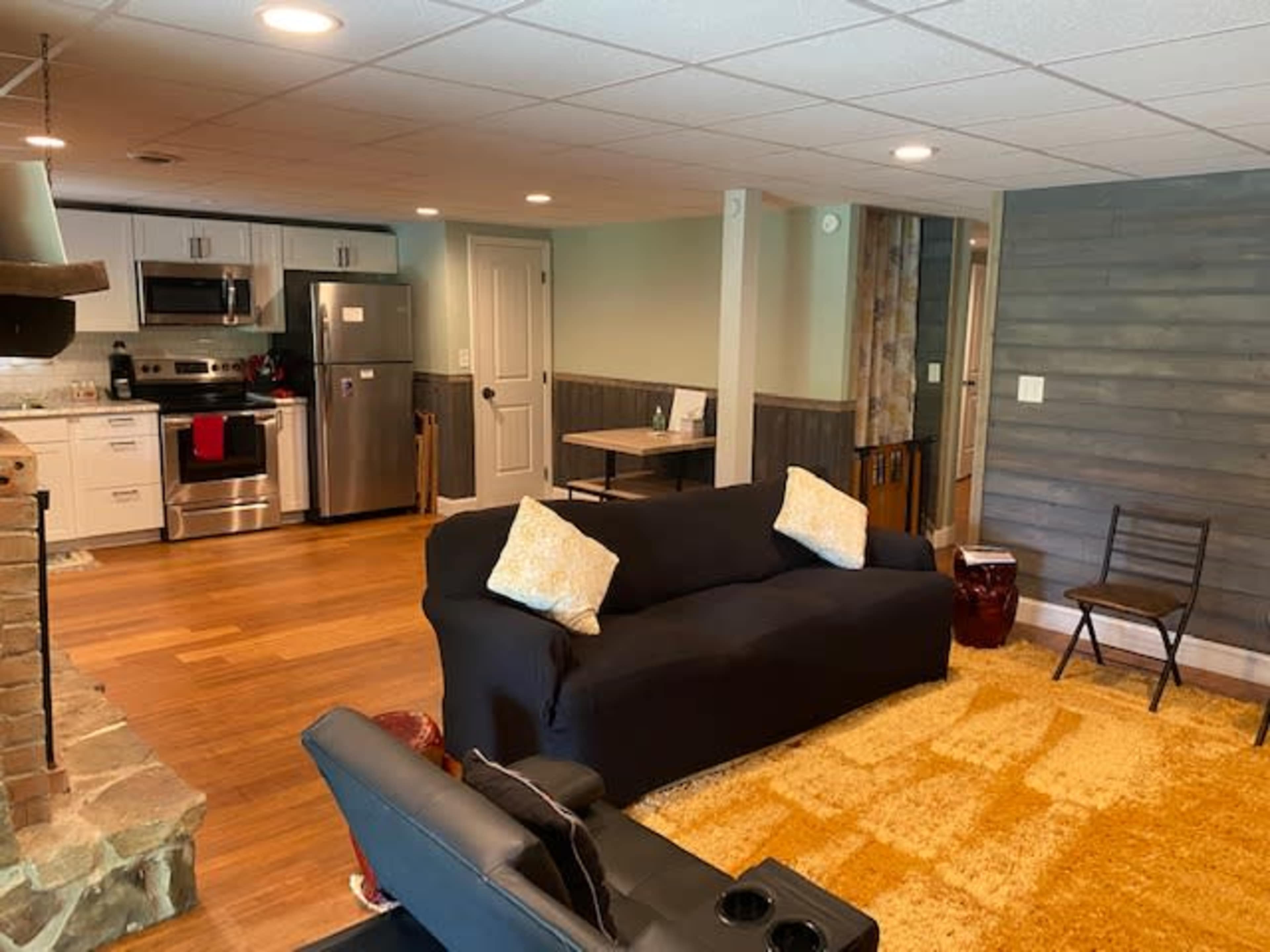 A finished basement area with a comfortable seating arrangement, a kitchenette with stainless steel appliances, and wooden flooring.