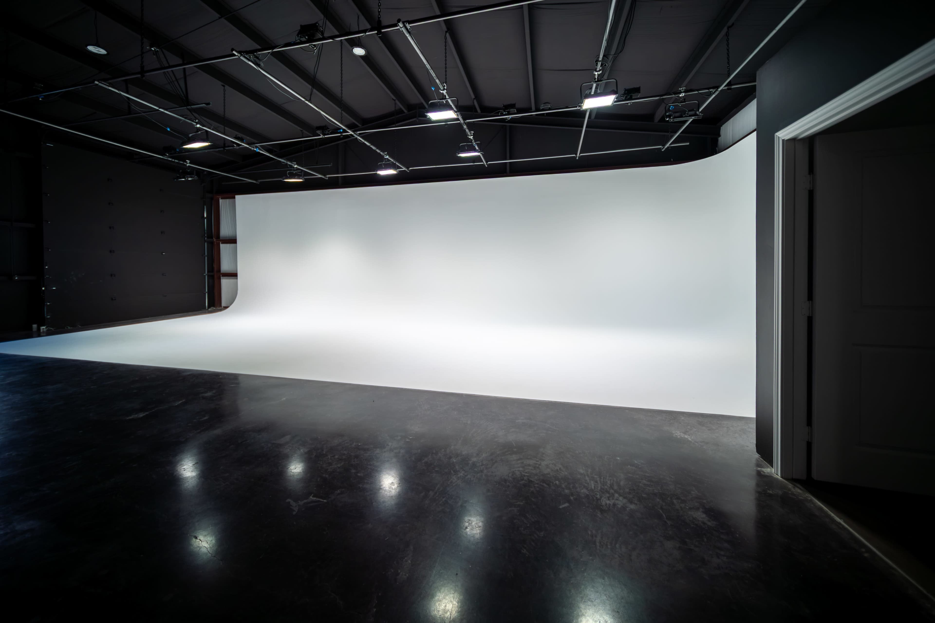 The image shows a spacious photography studio featuring a seamless white backdrop and polished dark floor.