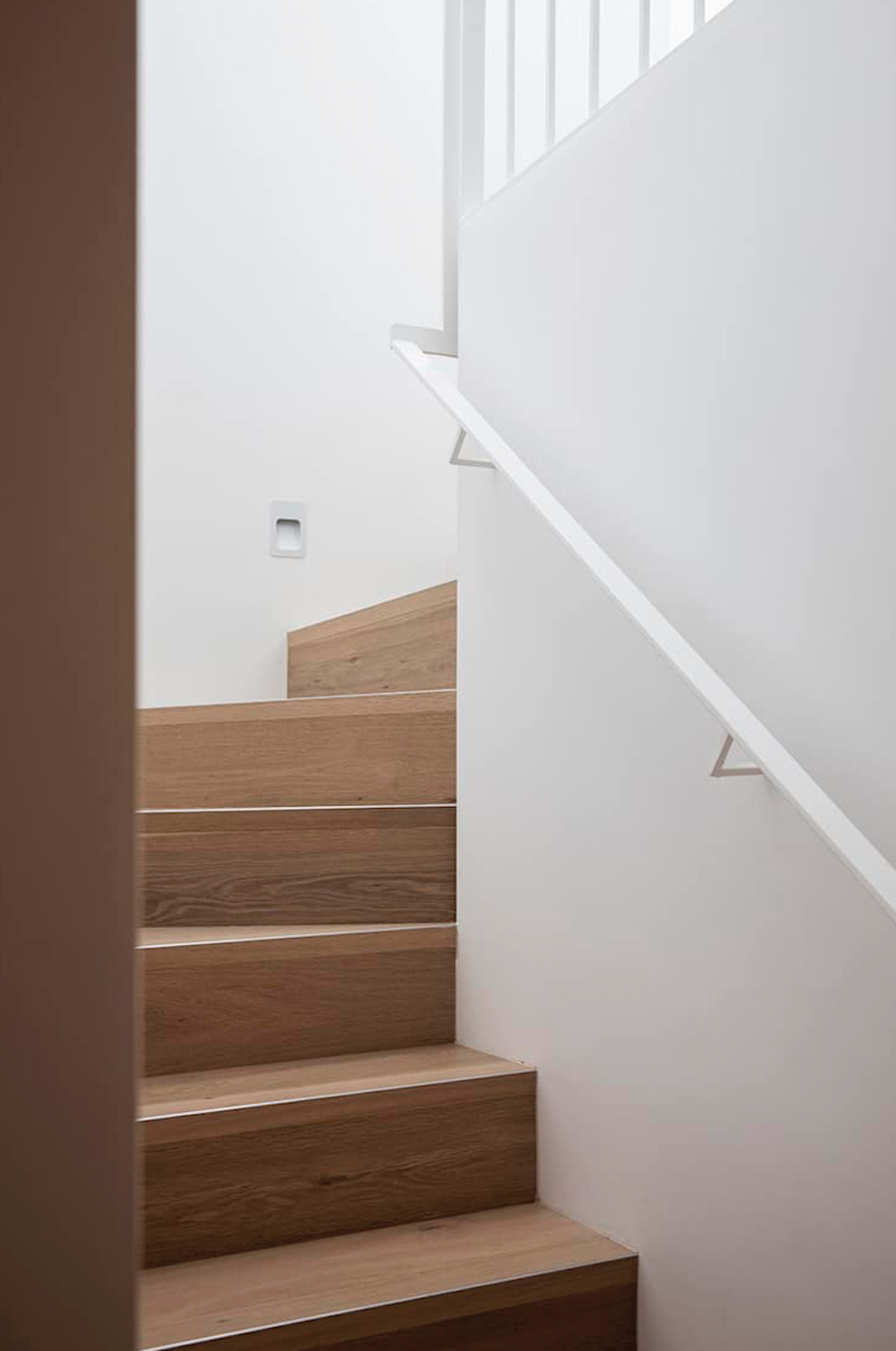 A set of wooden stairs ascending in a minimalistic white-walled space.