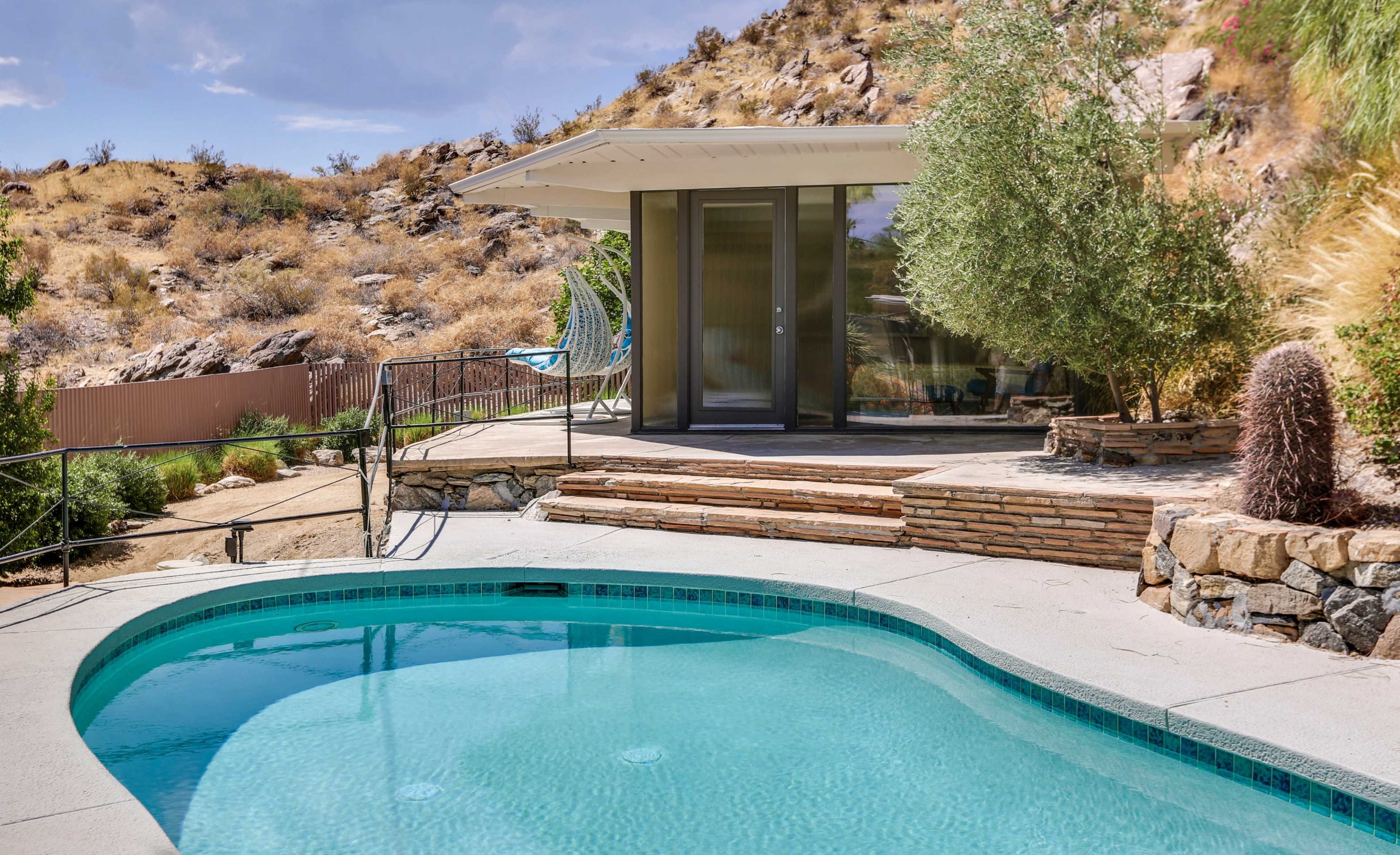 A swimming pool beside a modern house set against a hilly, arid landscape.