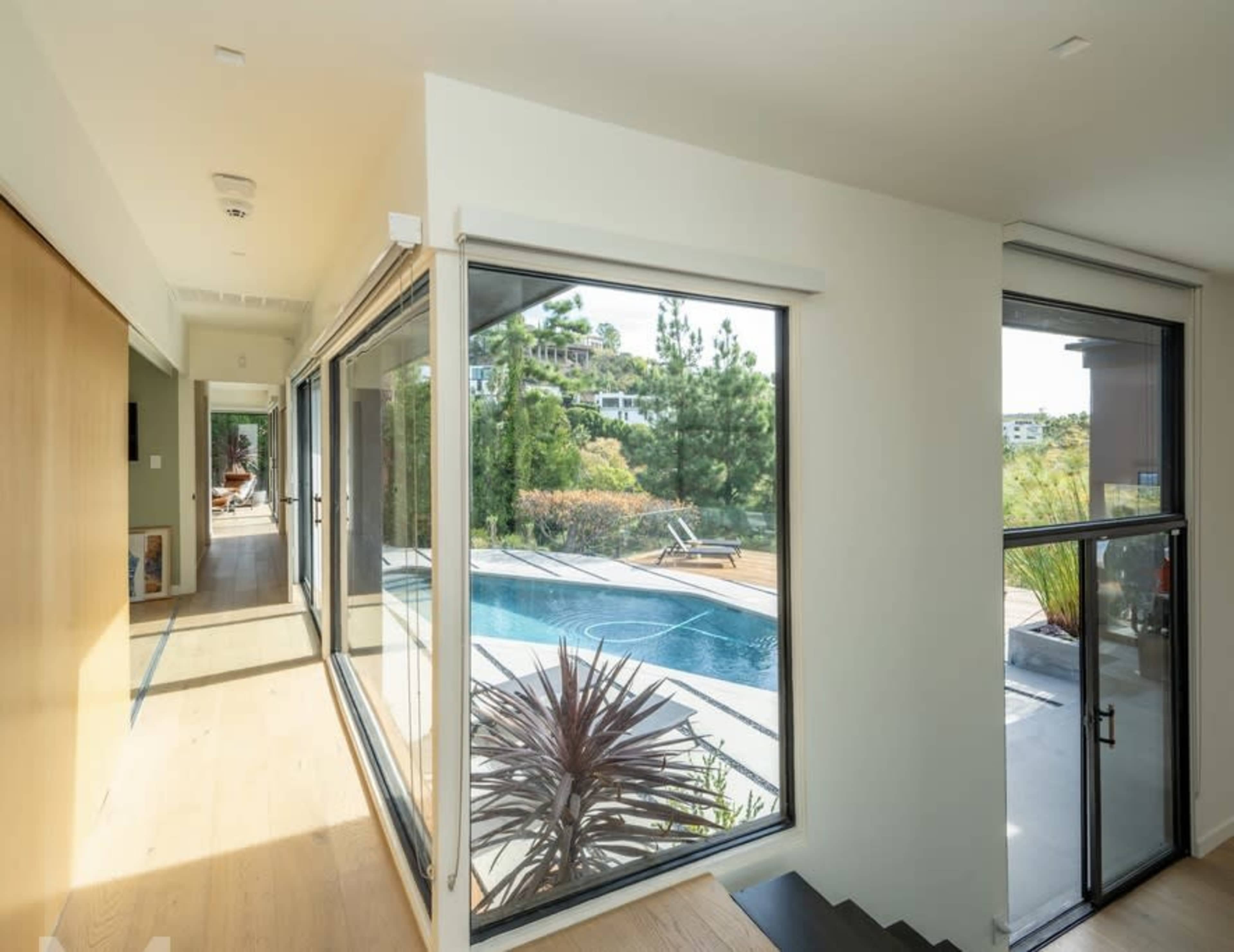 A modern hallway with large windows overlooks a swimming pool and landscaped greenery outside.