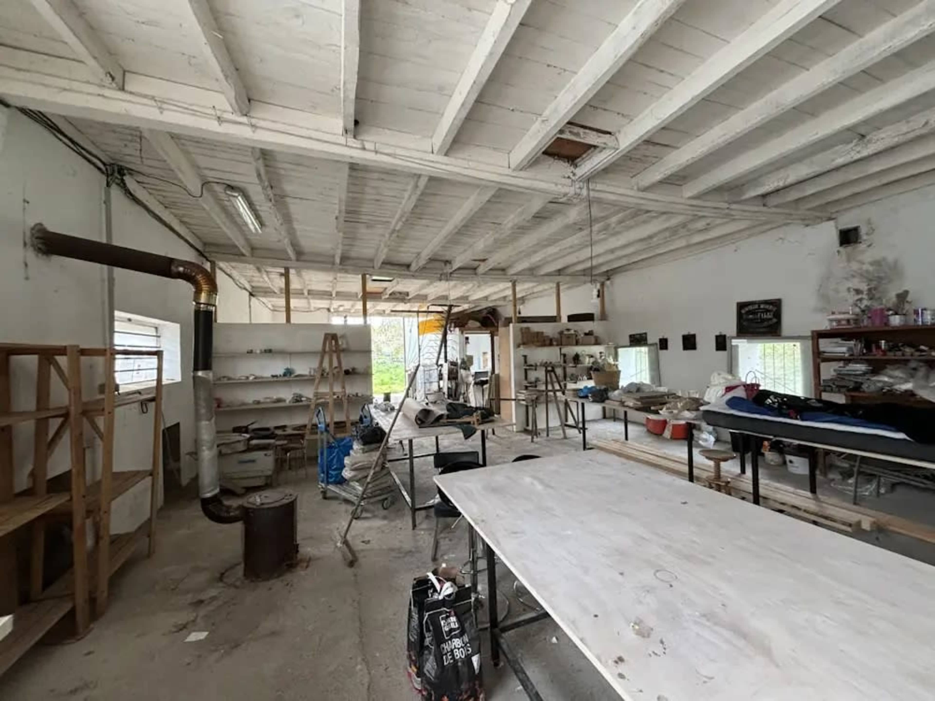 The image shows a spacious, unfinished workshop with wooden beams, various workstations, and tools scattered around.