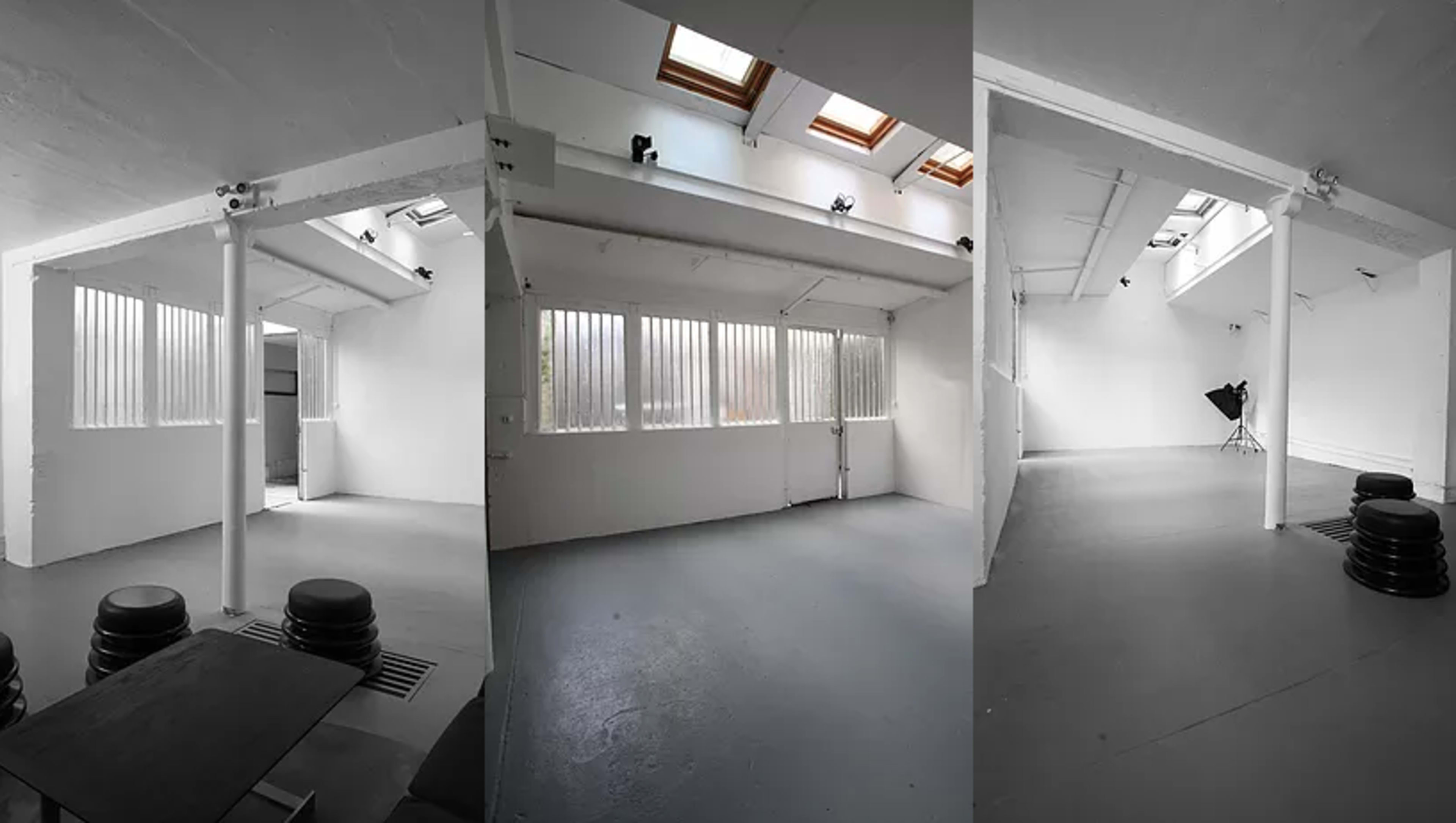 A spacious, bright studio with high ceilings, skylights, and large windows, featuring minimal furnishings and a gray floor.
