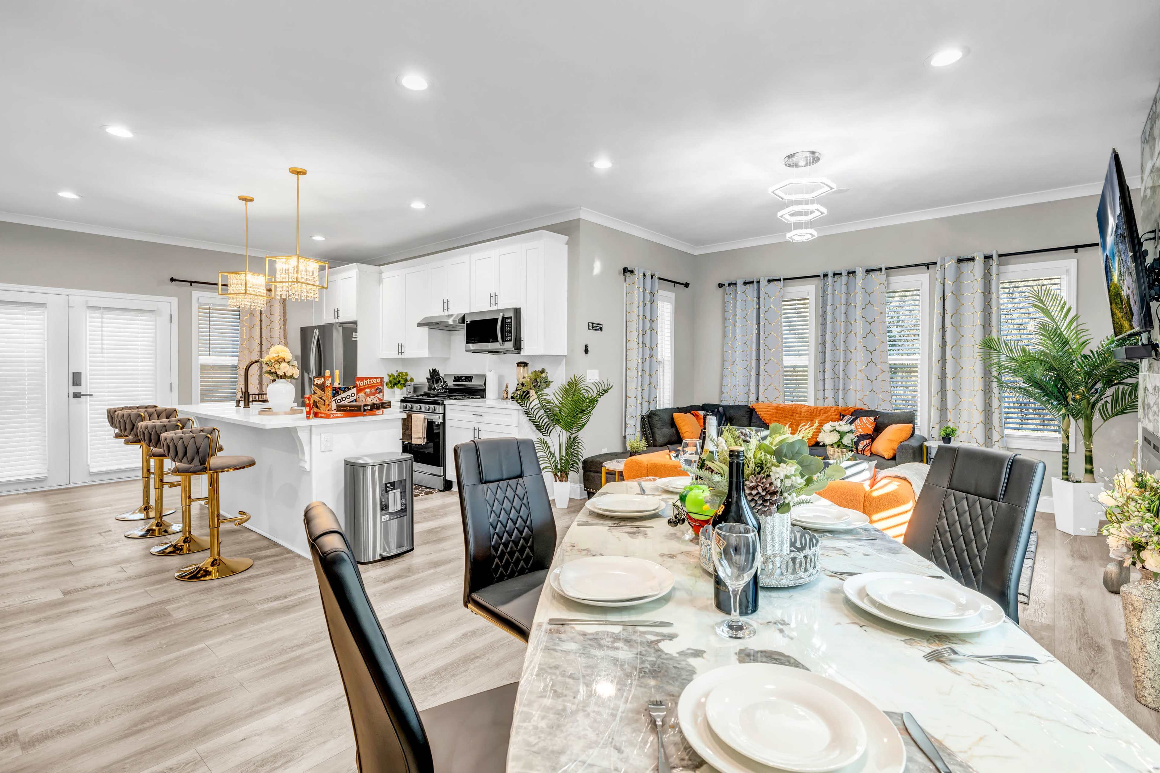The image shows a modern open-concept living area and dining space featuring a well-decorated kitchen, a dining table set for a meal, and a cozy seating area.