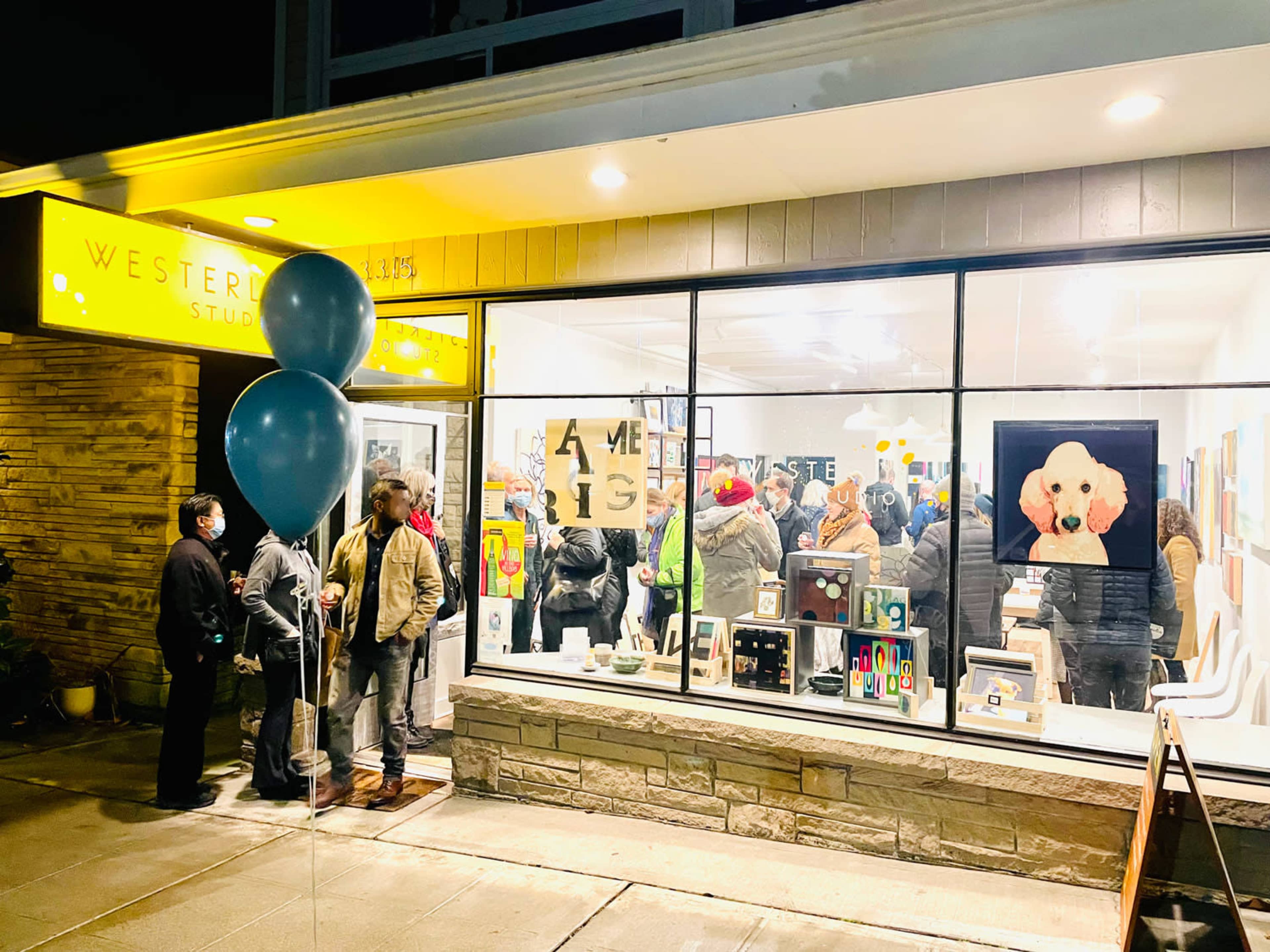 A crowd gathers outside Westerly Studios, with colorful artwork visible through the windows and blue balloons at the entrance.